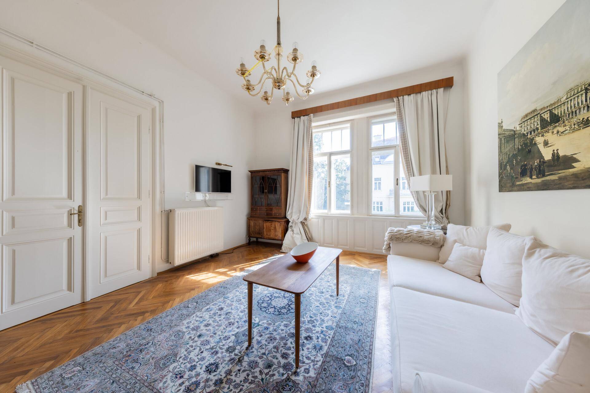Helles Wohnzimmer mit Parkettboden, großem Fenster und traditionellem Kachelofen.