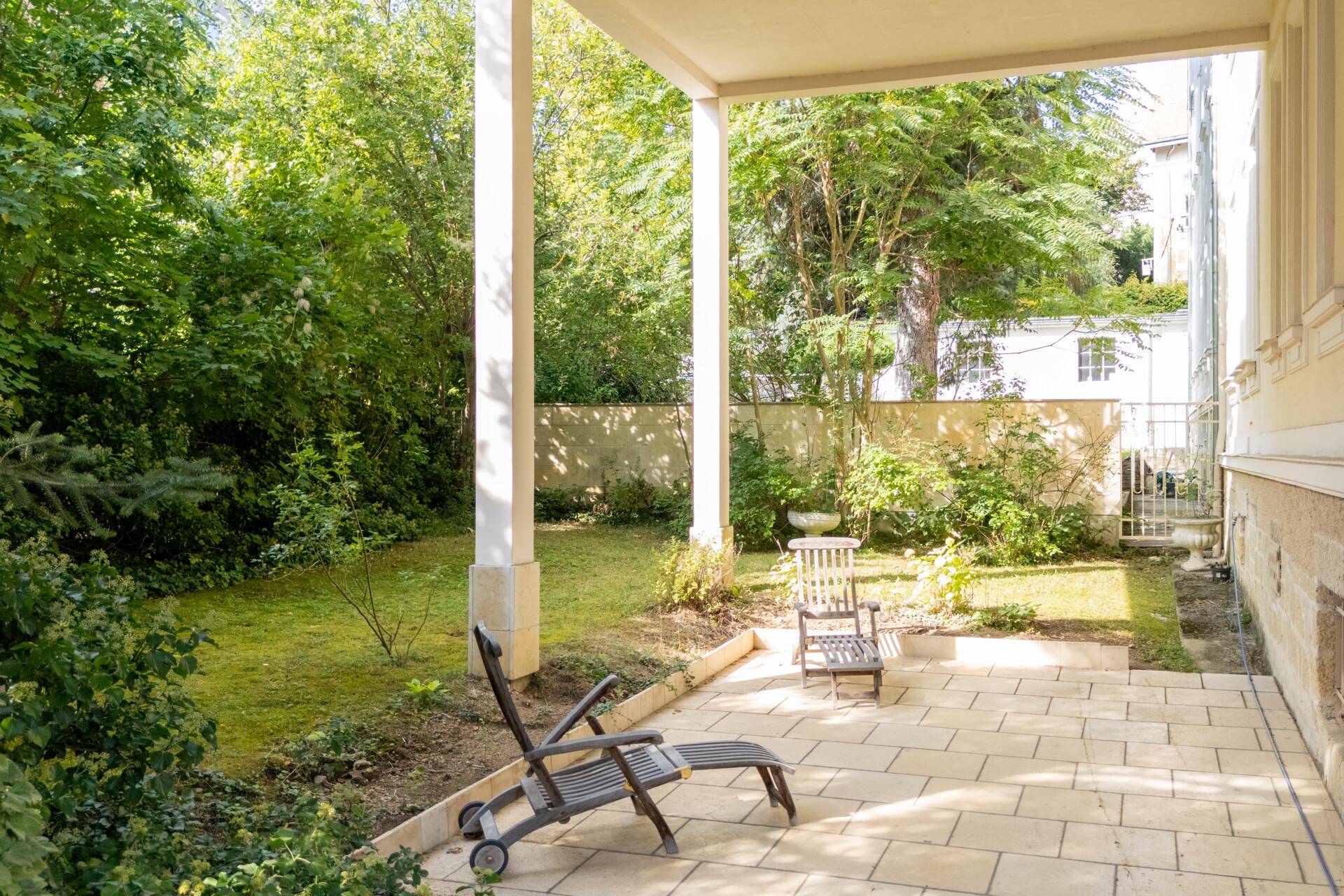 Grüner Gartenbereich mit überdachter Terrasse und Liegestuhl, ideal zum Entspannen.