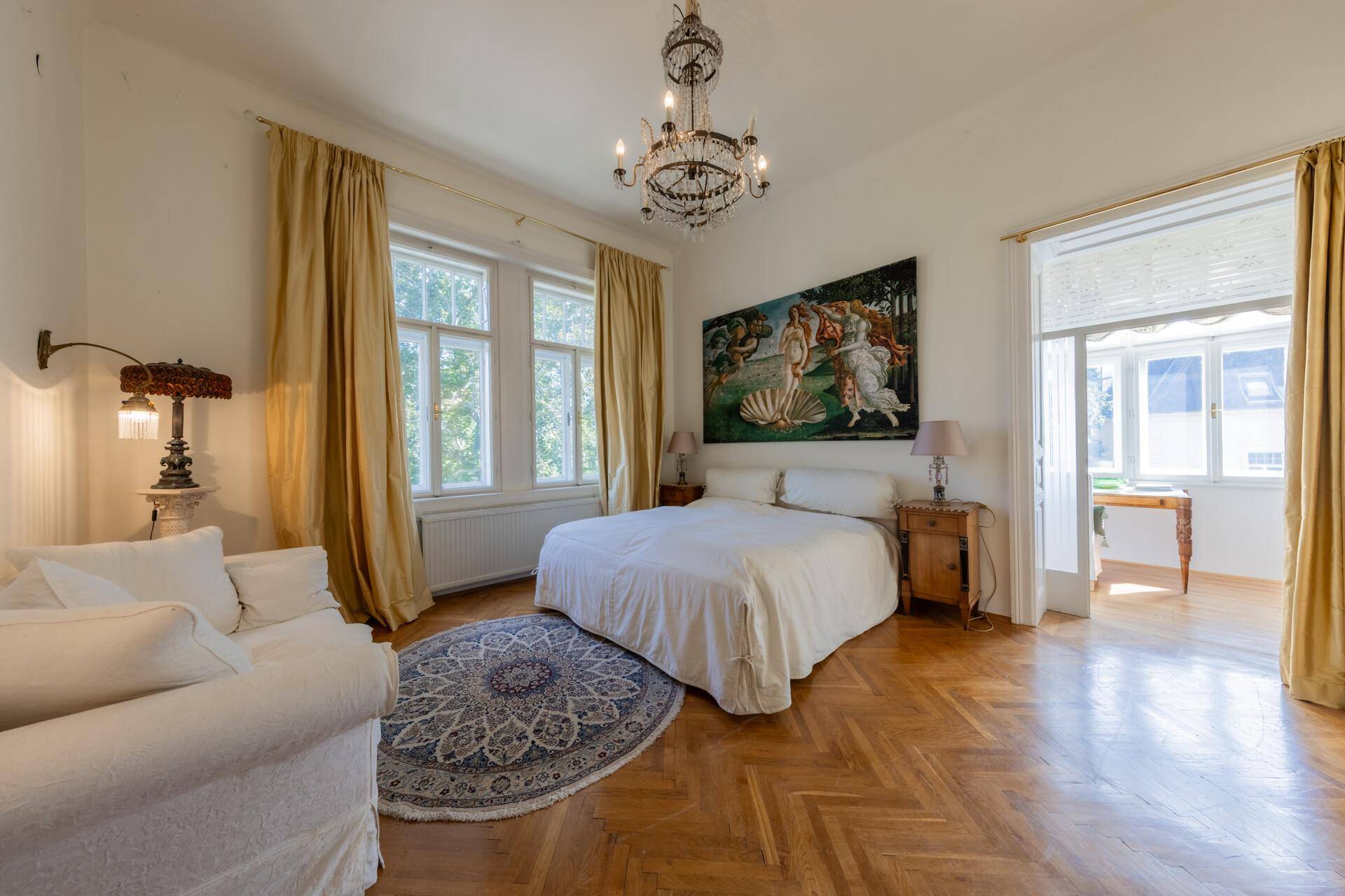 Geräumiges Schlafzimmer mit Parkettboden, Kamin und Zugang zu einem hellen Nebenraum.