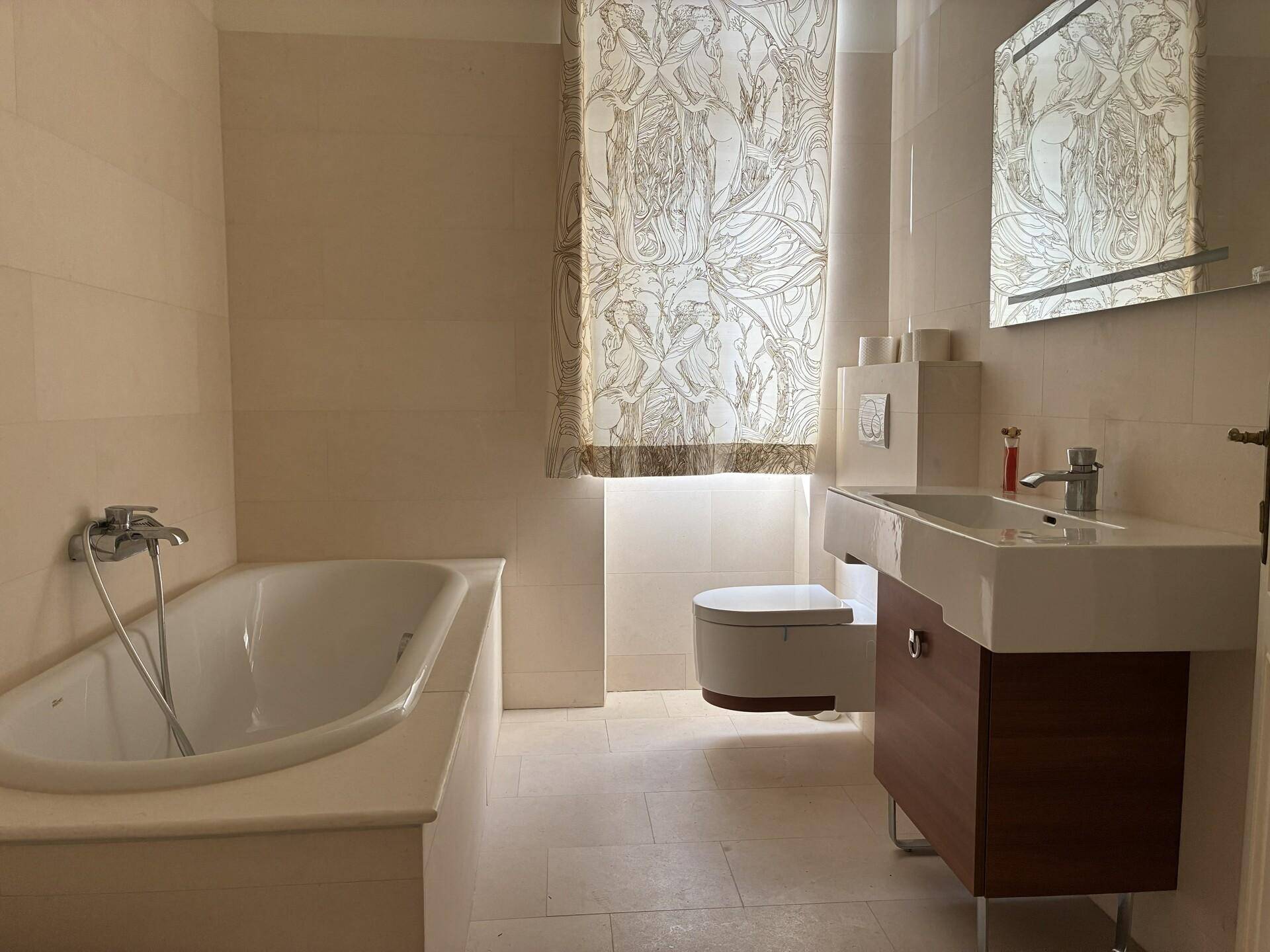 Modernes Badezimmer mit Badewanne, wandhängendem WC und großformatigen Fliesen.