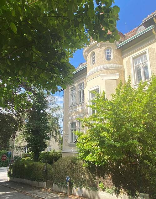 Elegante Stadtvilla mit historischer Architektur, umgeben von üppigem Grün und Bäumen.