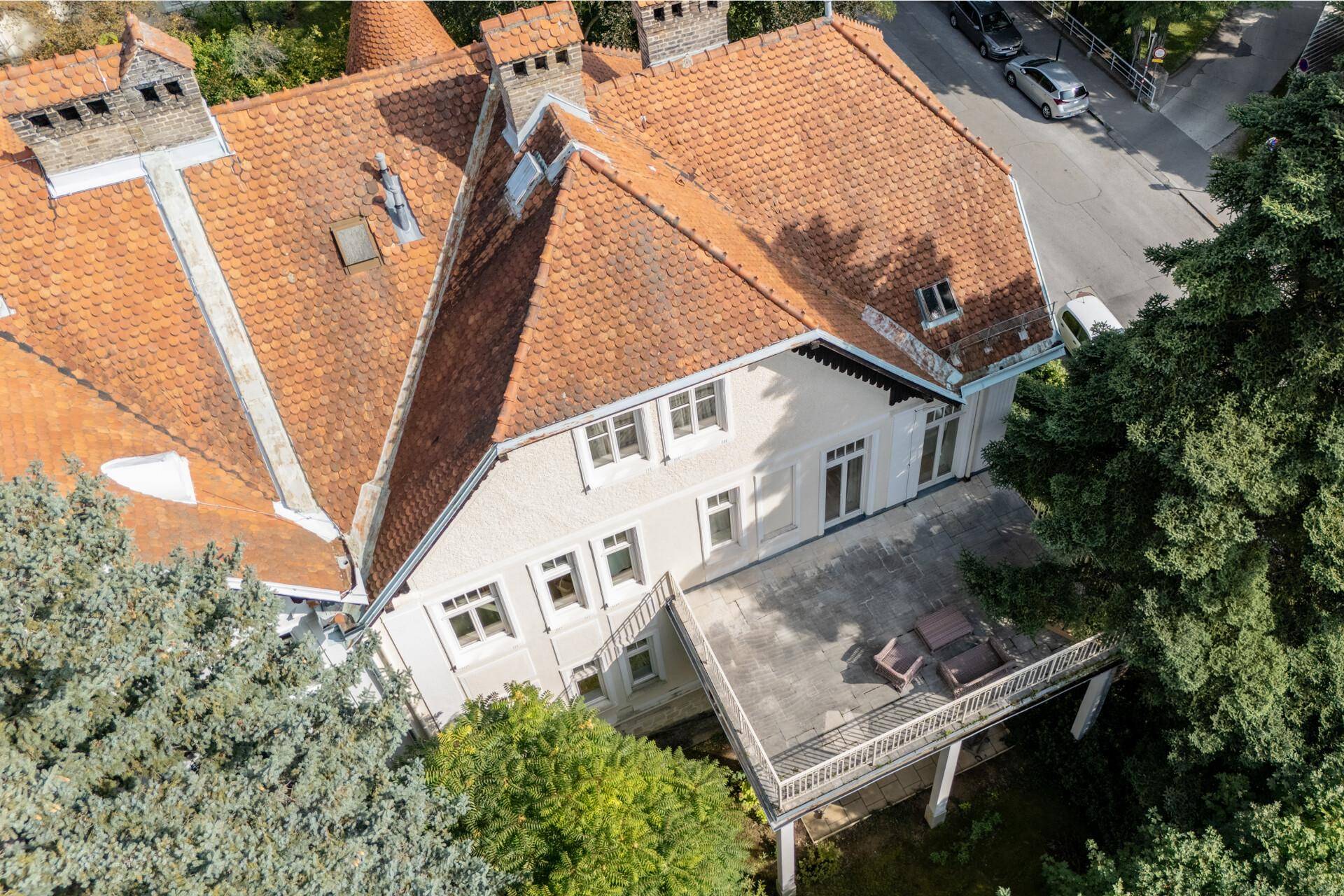 Dachansicht der Villa mit großer Terrasse und Sitzgelegenheiten, umgeben von hohen Bäumen.