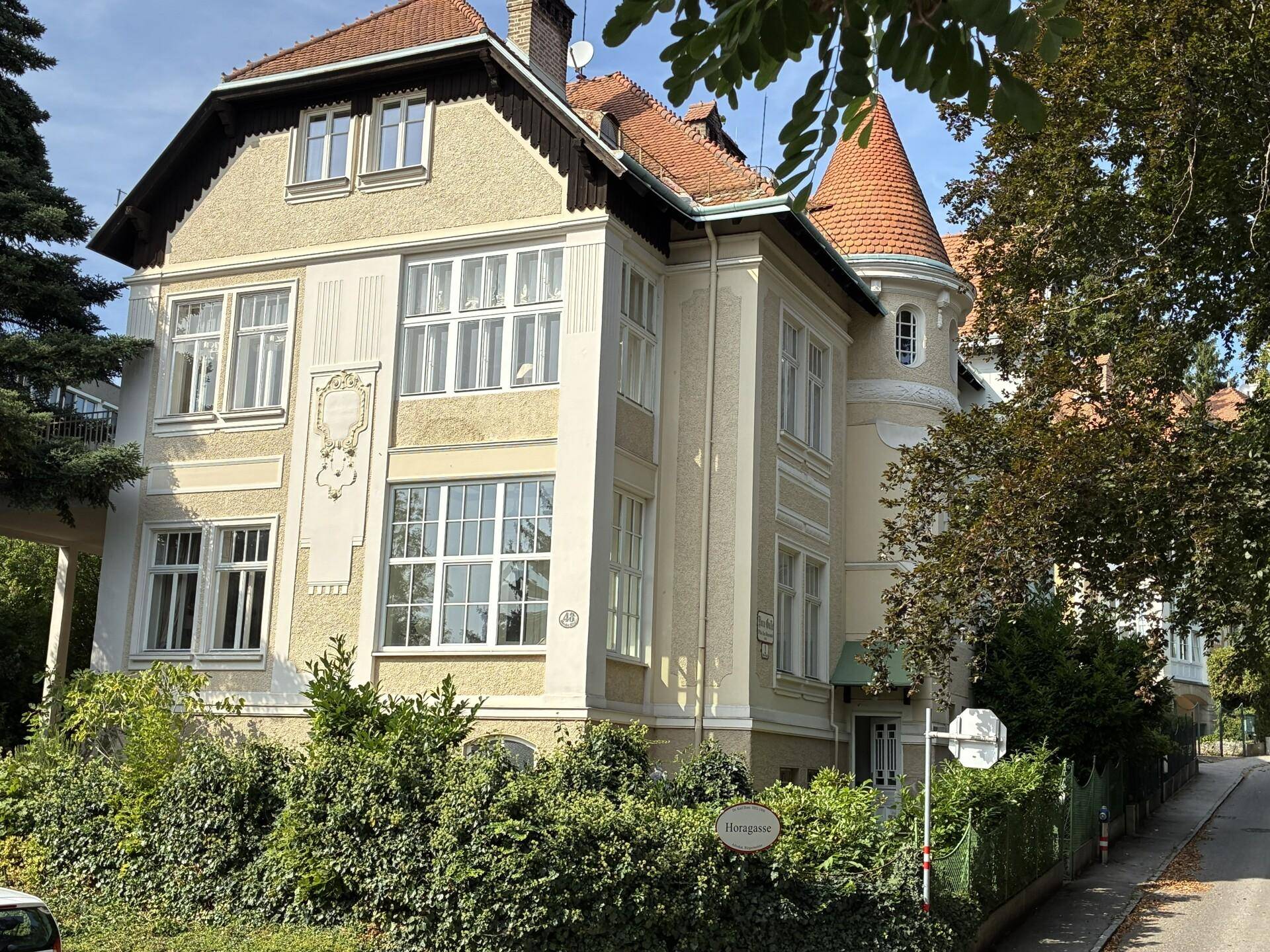 Historische Villa mit markanter Architektur und üppigem Grün umgeben.