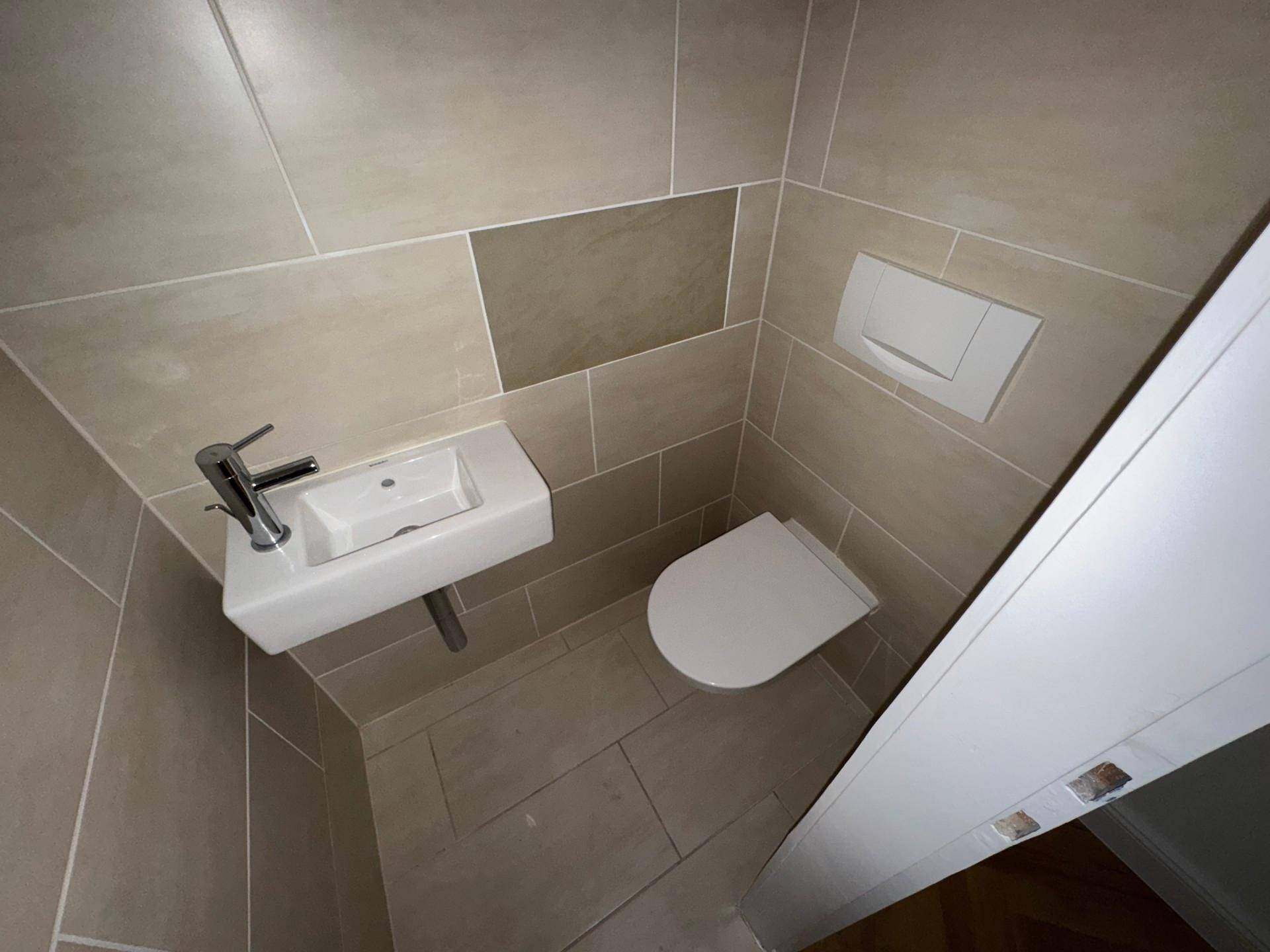 Modern gefliestes Gäste-WC mit wandhängendem WC und kleinem Handwaschbecken.