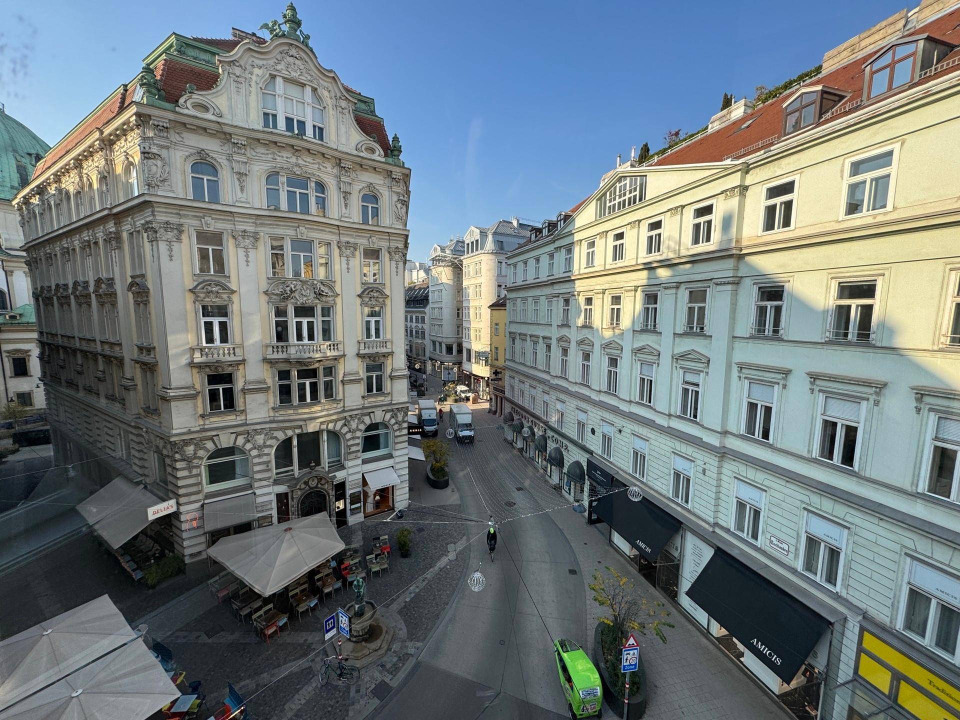 Panoramablick auf eine belebte Stadtstraße mit historischen Gebäuden und Geschäften unter blauem Himmel.