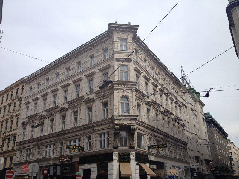 Historisches Eckgebäude mit reich verzierter Fassade und großen Fenstern in einer städtischen Umgebung.