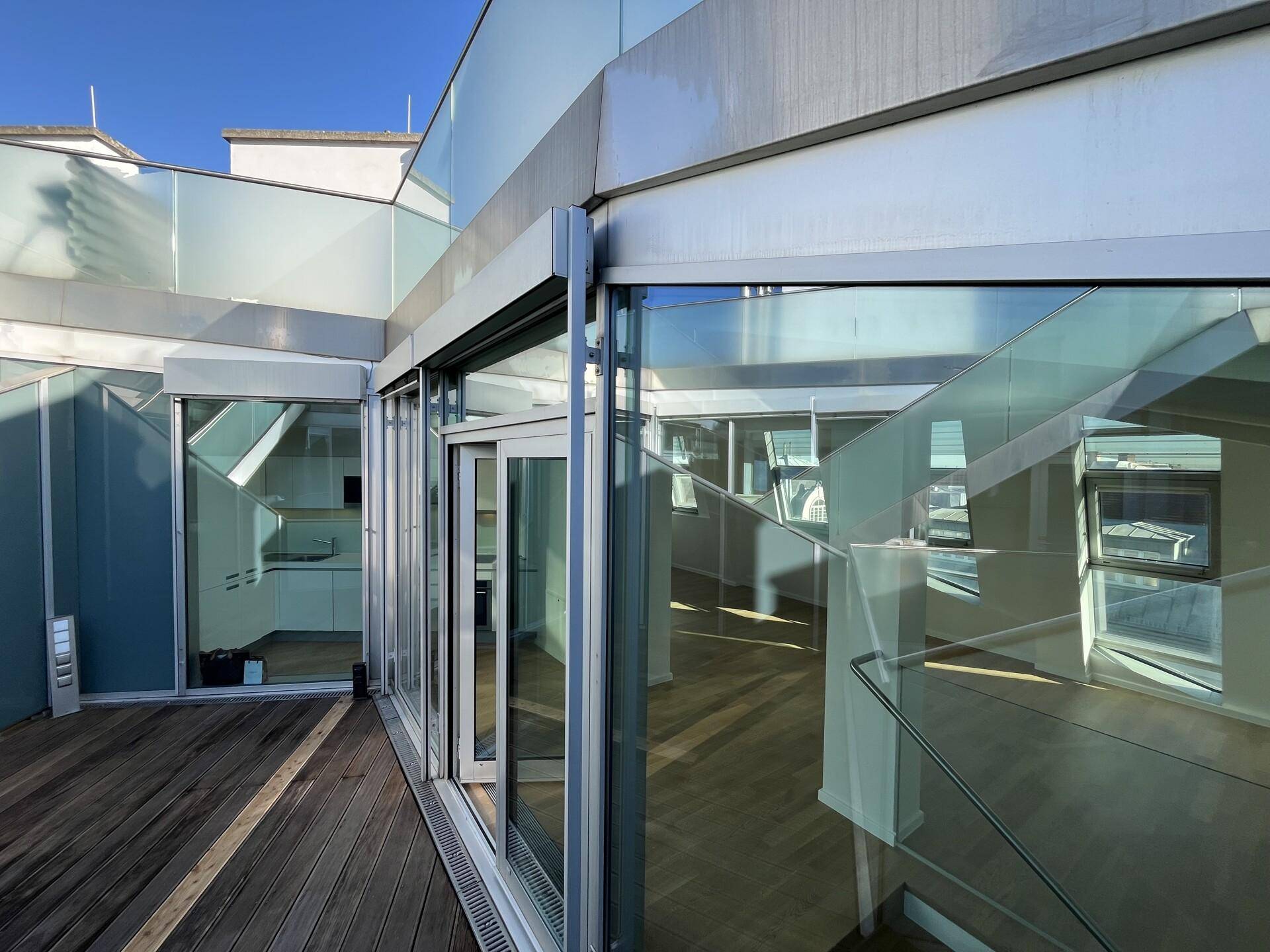 Geräumige Dachterrasse mit Holzbelag und großen Glasfronten, die den Innenraum verbinden.