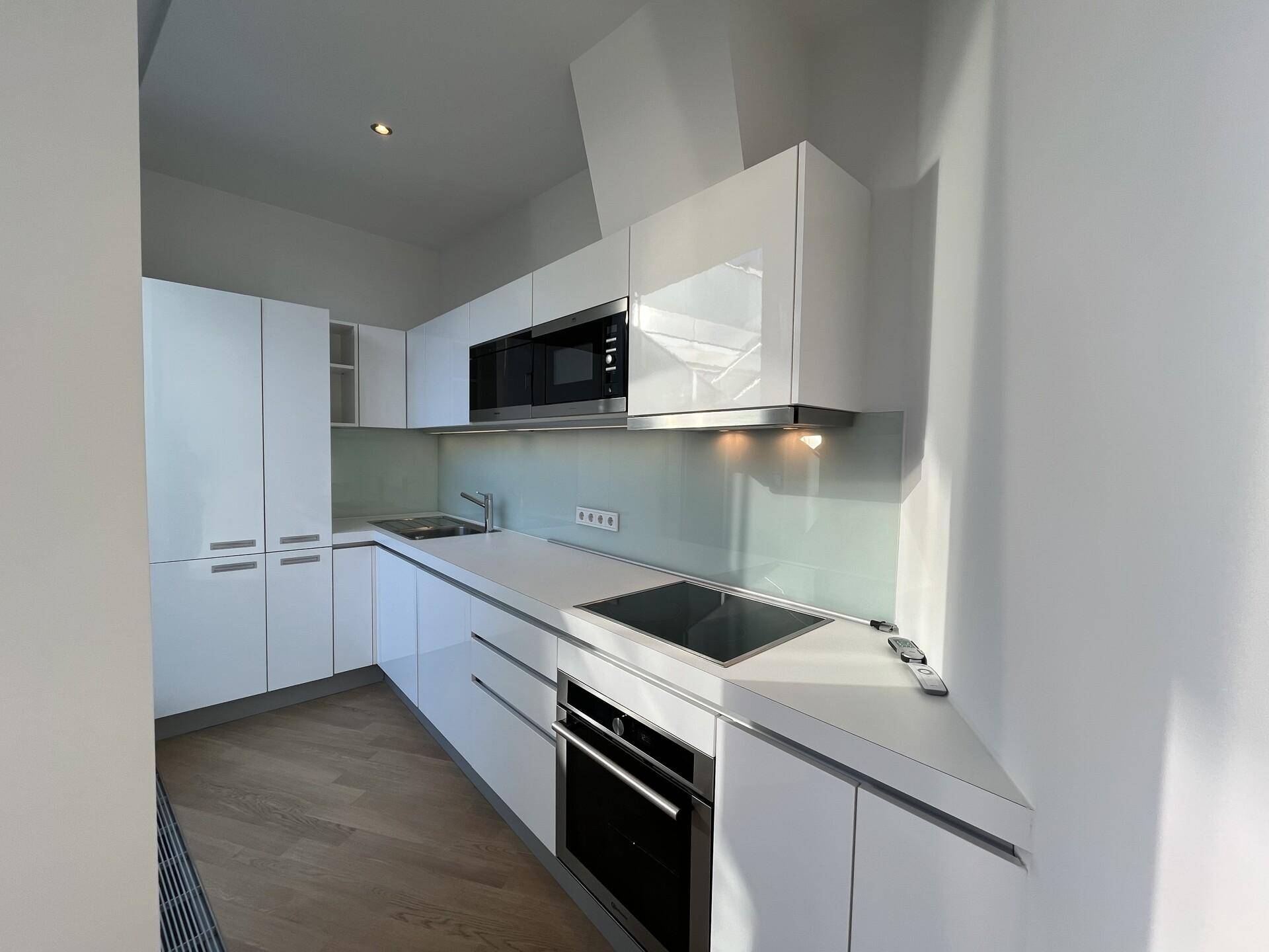 Moderne Einbauküche mit weißen Hochglanzfronten, Induktionskochfeld und integrierten Geräten.