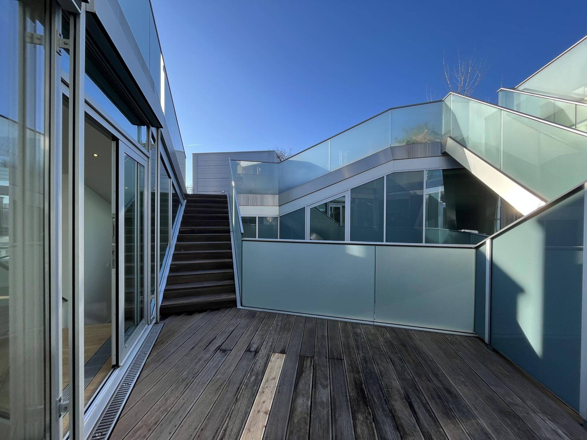 Mehrstufige Dachterrasse mit Holzbelag, Glasgeländern und moderner Architektur.