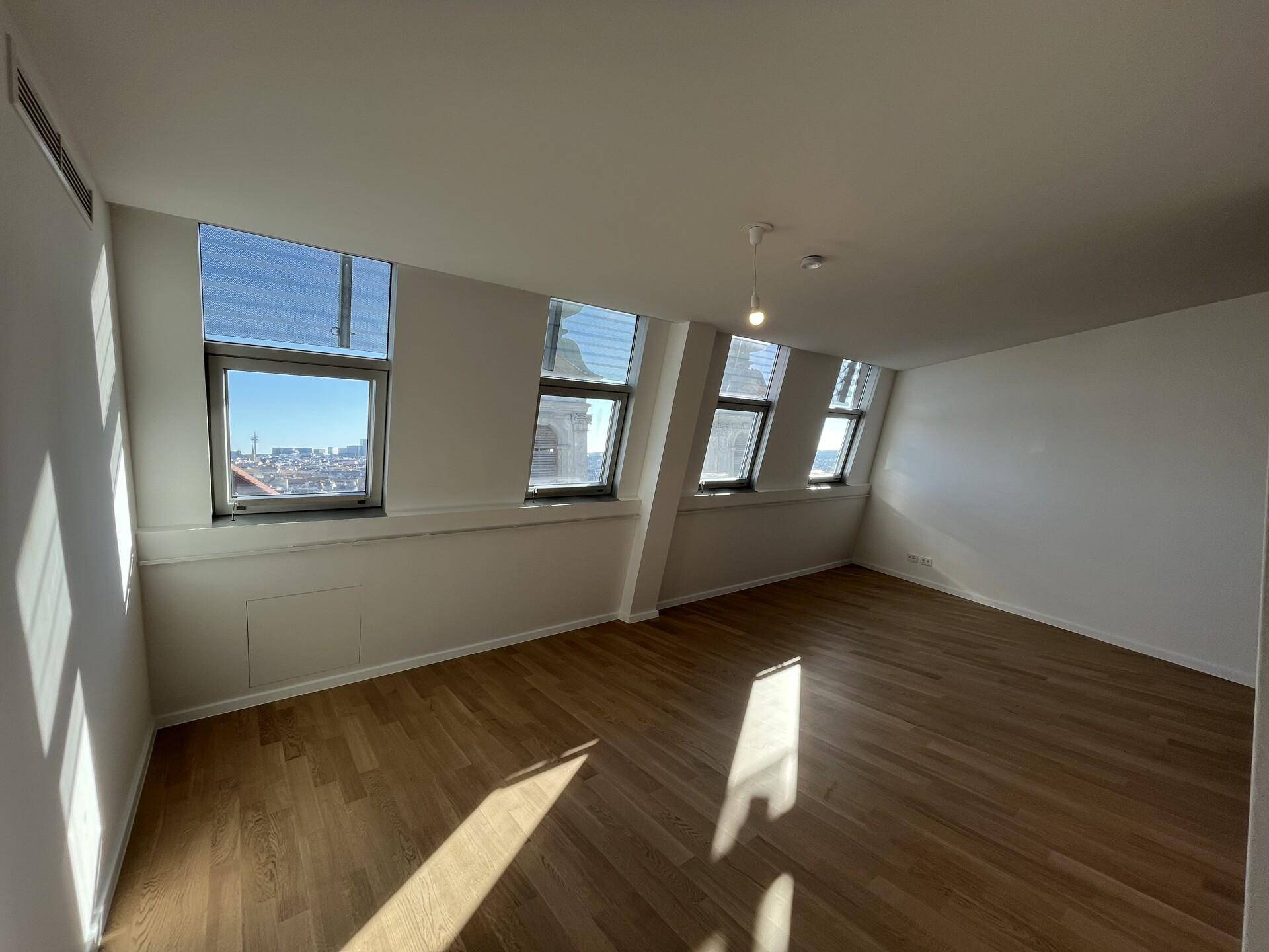 Heller, leerer Raum mit Holzboden und schrägen Fenstern, ideal als Schlafzimmer.