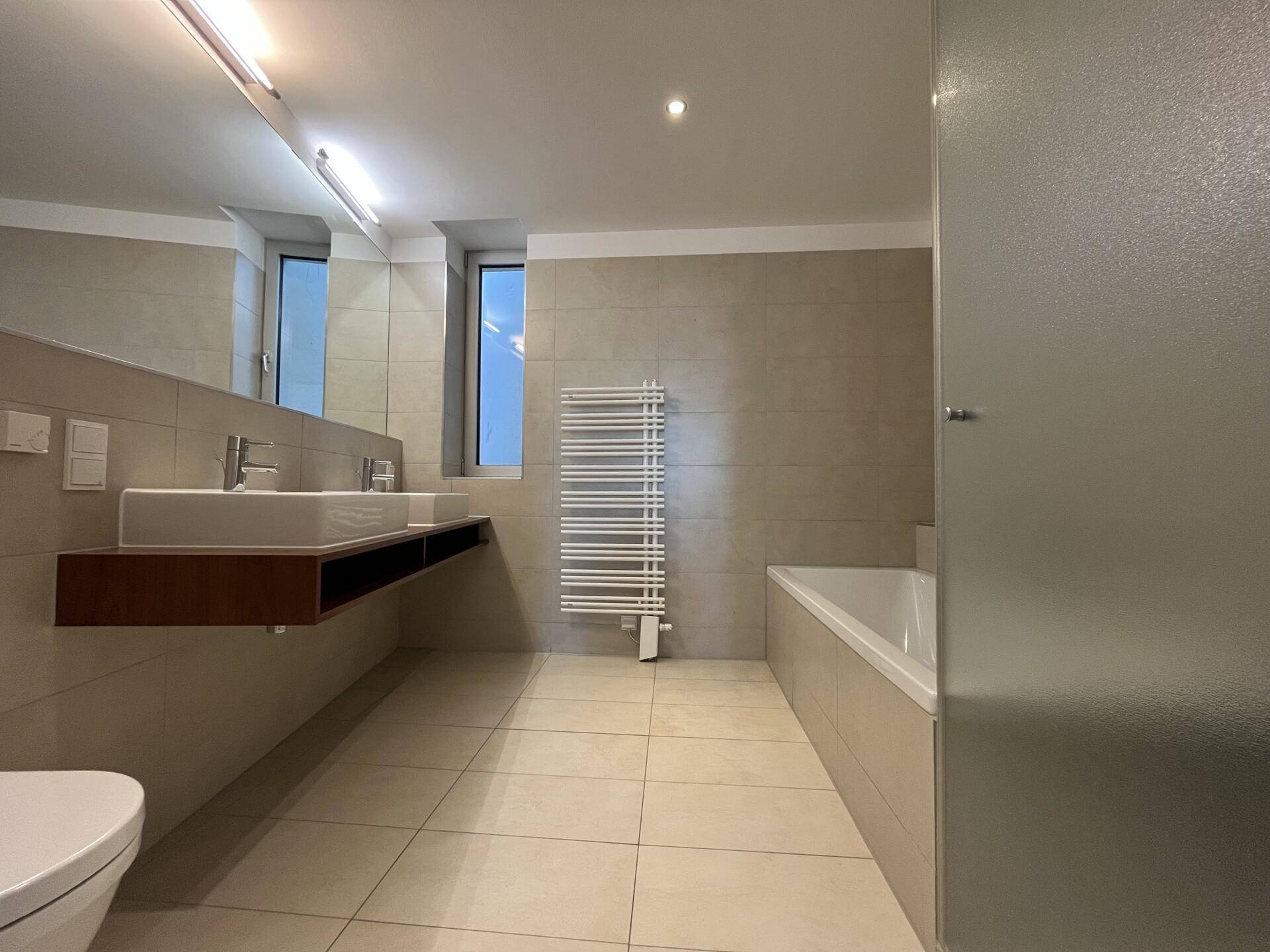 Geräumiges Badezimmer mit Doppelwaschbecken, Badewanne und beheiztem Handtuchhalter.