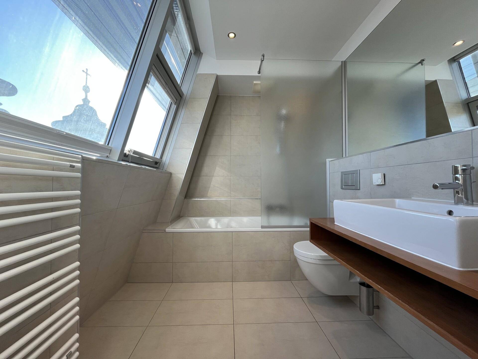 Modernes Badezimmer mit Badewanne, Dusche, Waschtisch und schrägen Dachfenstern.