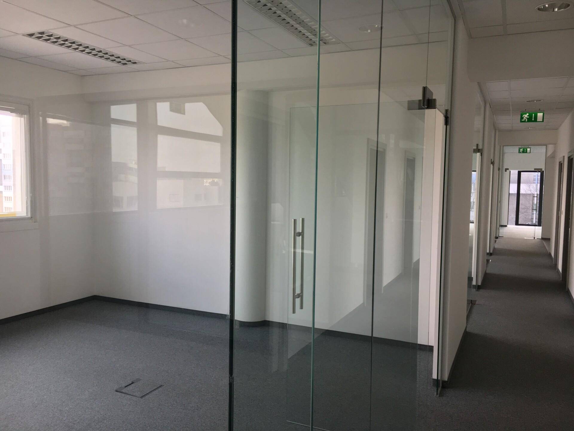 Leeres Büro mit Glaswänden, Teppichboden und natürlichem Lichteinfall durch die Fenster.