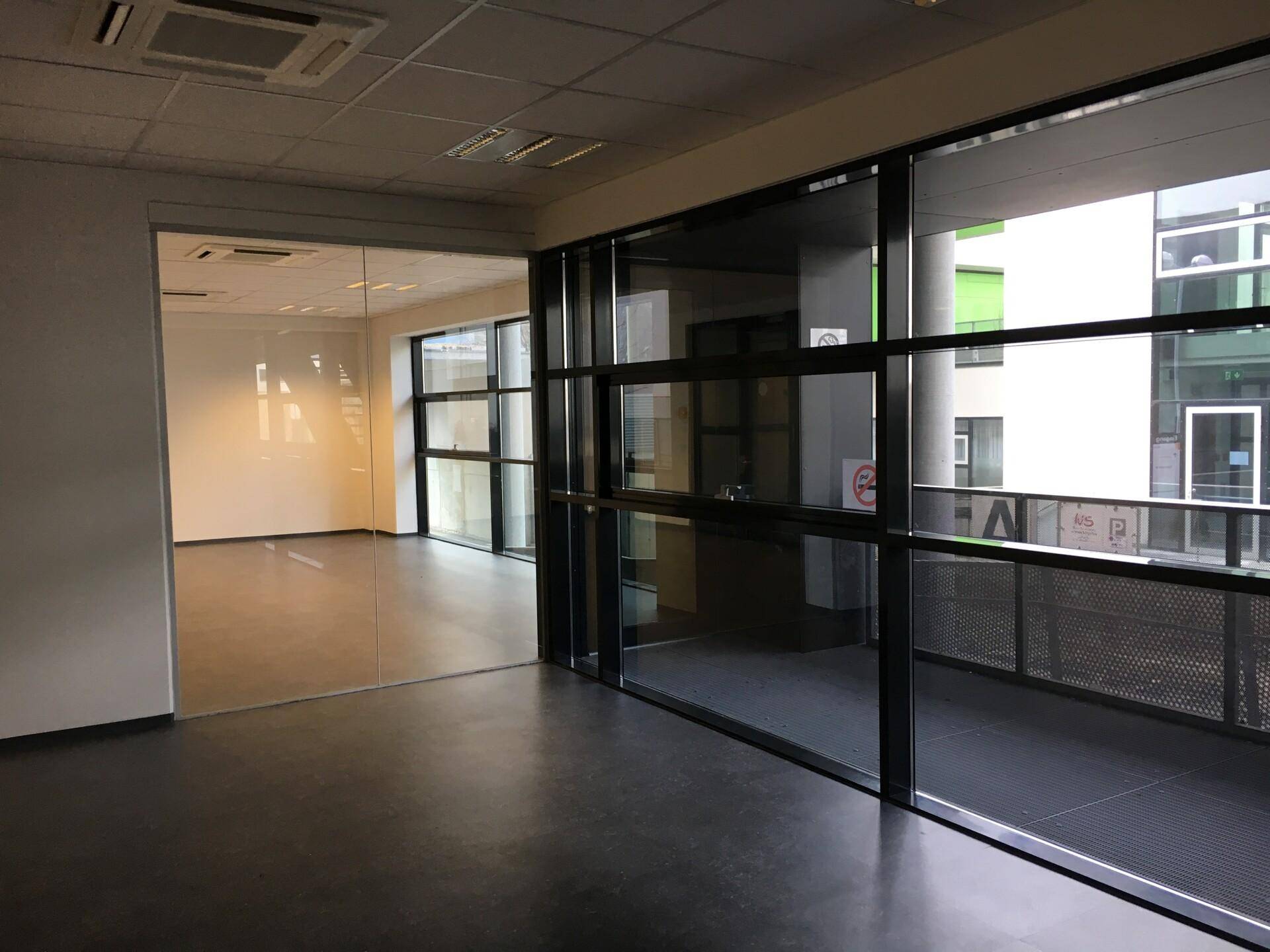 Moderner Bürobereich mit Glaswänden und großen Fenstern, die viel Tageslicht hereinlassen.