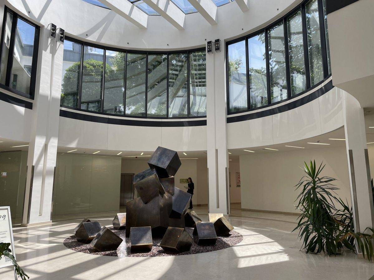 Helle, mehrstöckige Lobby mit einem großen Oberlicht, geschwungenen Glasfronten und einer modernen Skulptur.