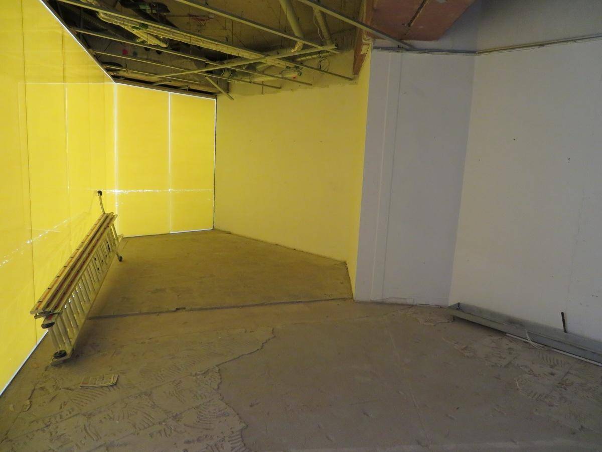 Unfertiger Raum mit gelben Schutzwänden und rohem Betonboden, bereit für den weiteren Ausbau.