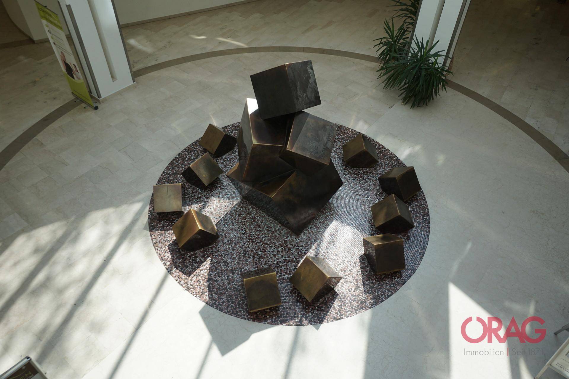 Blick von oben auf die zentrale Skulptur im Atrium mit kreisförmigem Bodenmuster.
