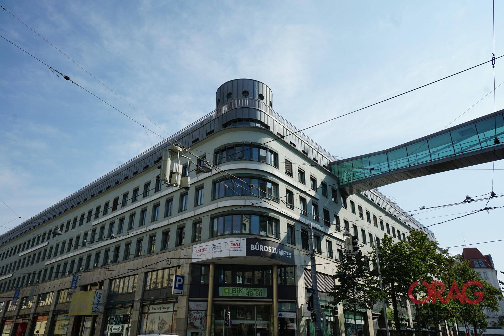 Moderne Bürogebäude-Fassade mit geschwungener Architektur und einer gläsernen Verbindungsbrücke.