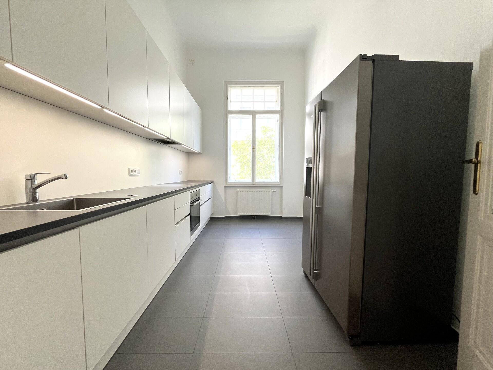 Moderne Küche mit weißen Schränken, dunkler Arbeitsplatte und großem Kühlschrank, ideal für kulinarische Aktivitäten.