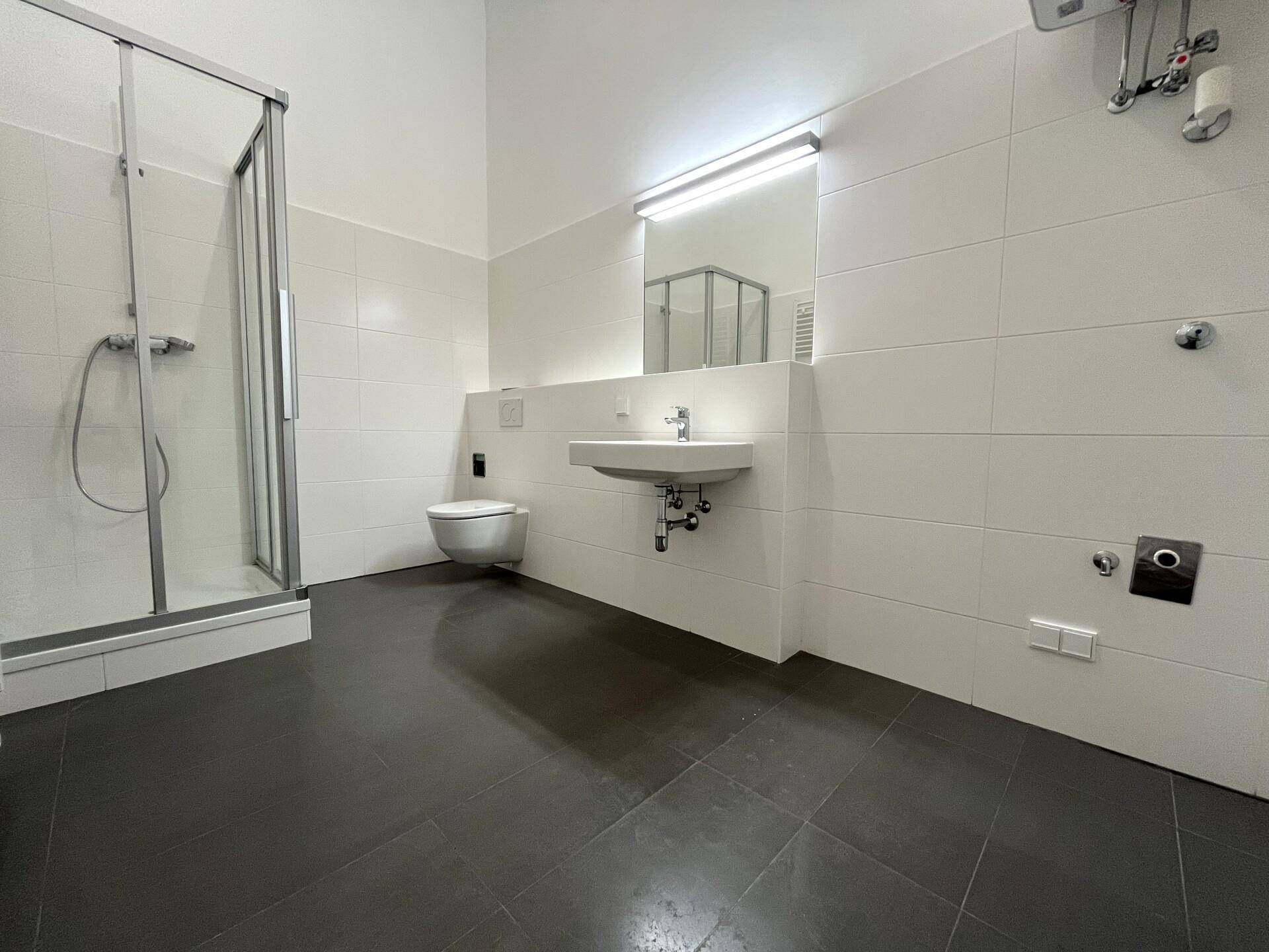 Modernes Badezimmer mit Duschkabine, wandhängendem WC und Waschbecken, alles in hellen Fliesen gehalten.