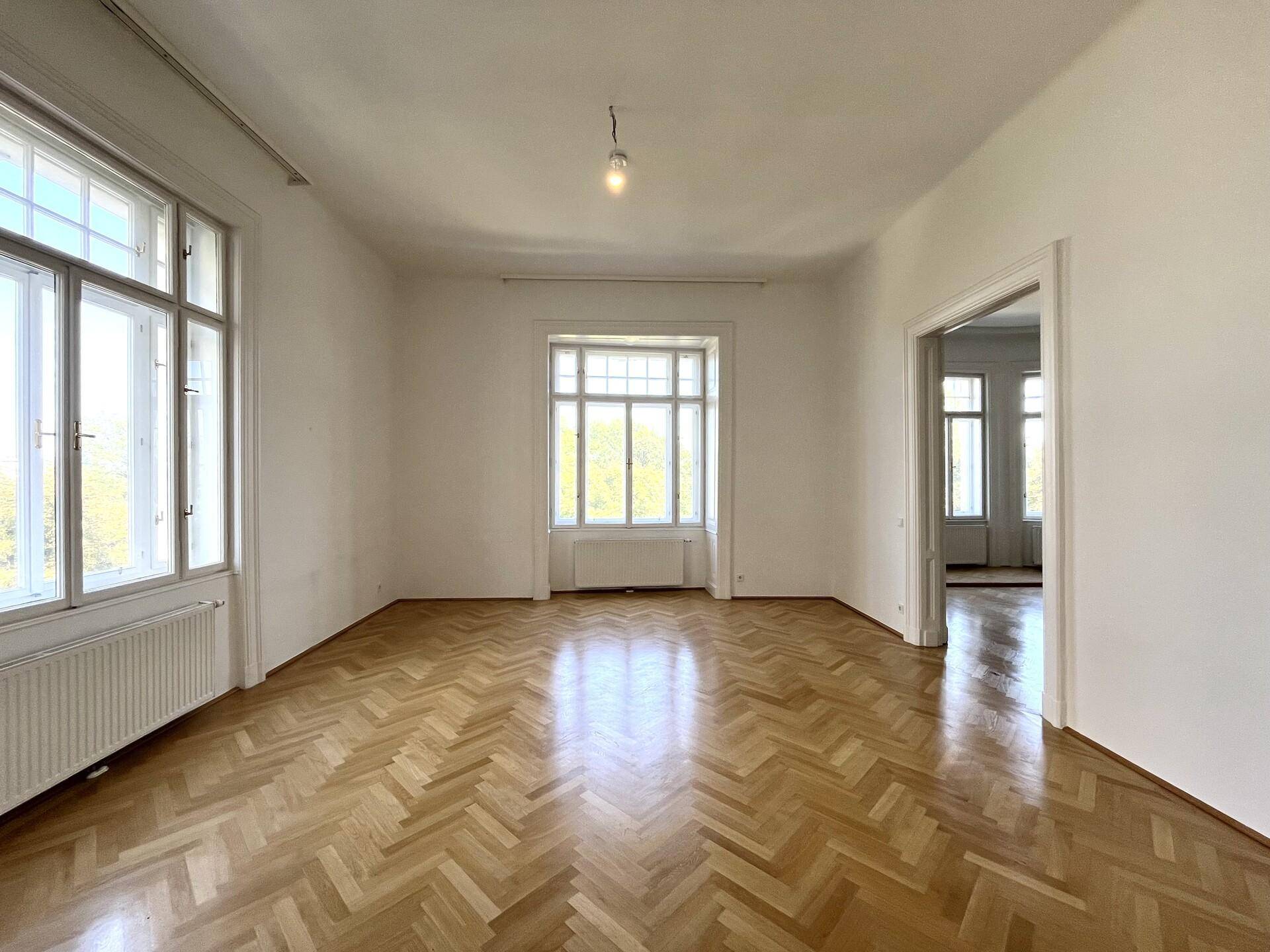 Helles Zimmer mit klassischem Fischgrätparkett und hohen Fenstern, die den Raum mit Licht füllen.
