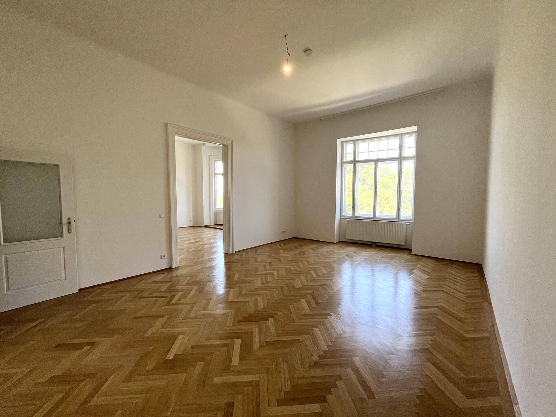 Geräumiges Zimmer mit glänzendem Fischgrätparkett und einem großen Fenster, das den Raum erhellt.