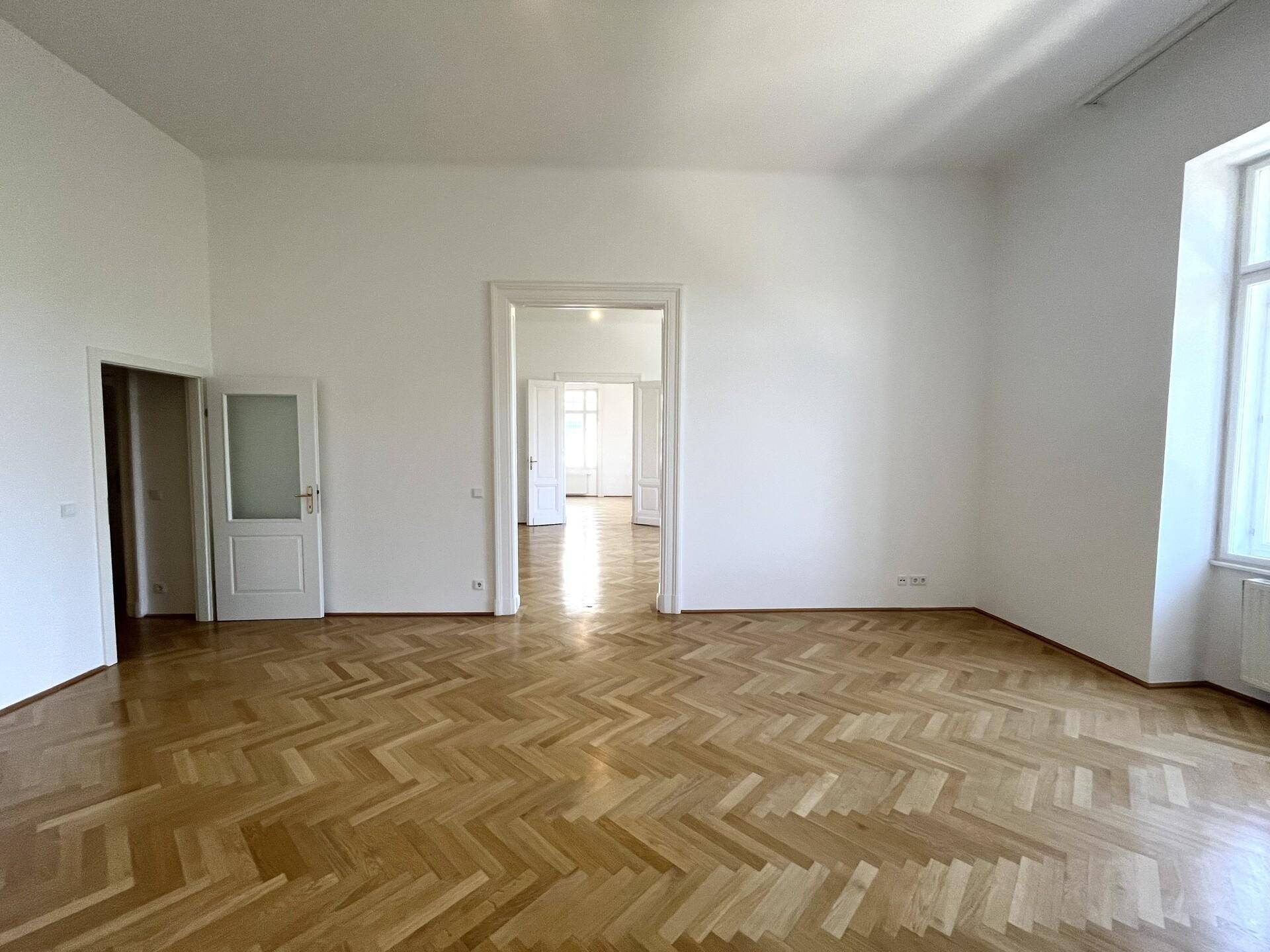 Geräumiges Zimmer mit glänzendem Fischgrätparkett und einem großen Fenster, das den Raum erhellt.