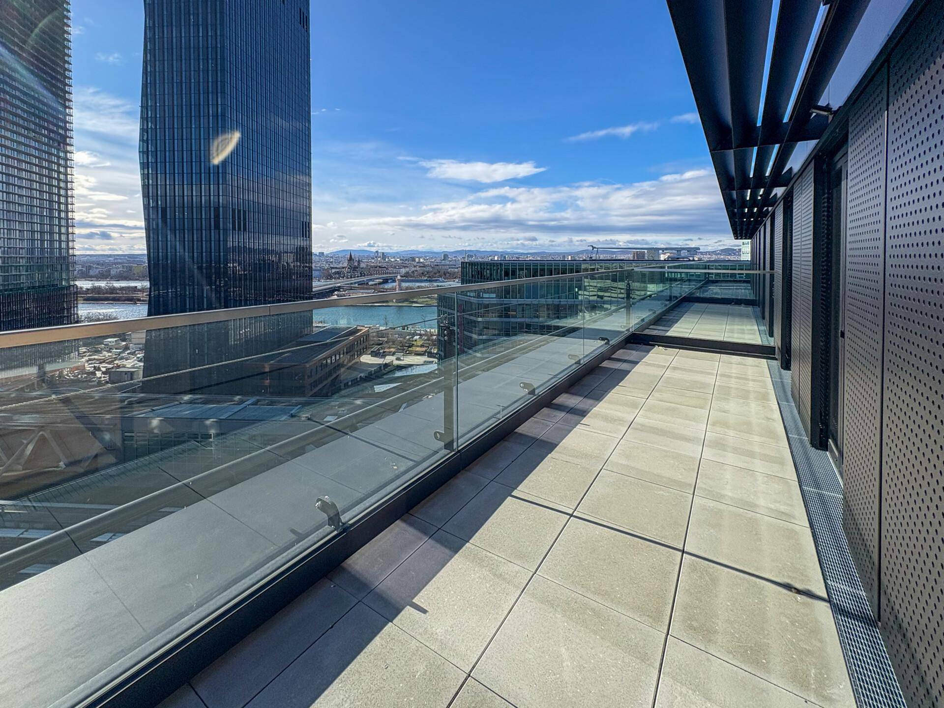 Weitläufige Dachterrasse mit Fliesenboden, Glasbrüstung und beeindruckendem Panoramablick auf die Stadt und den Fluss.