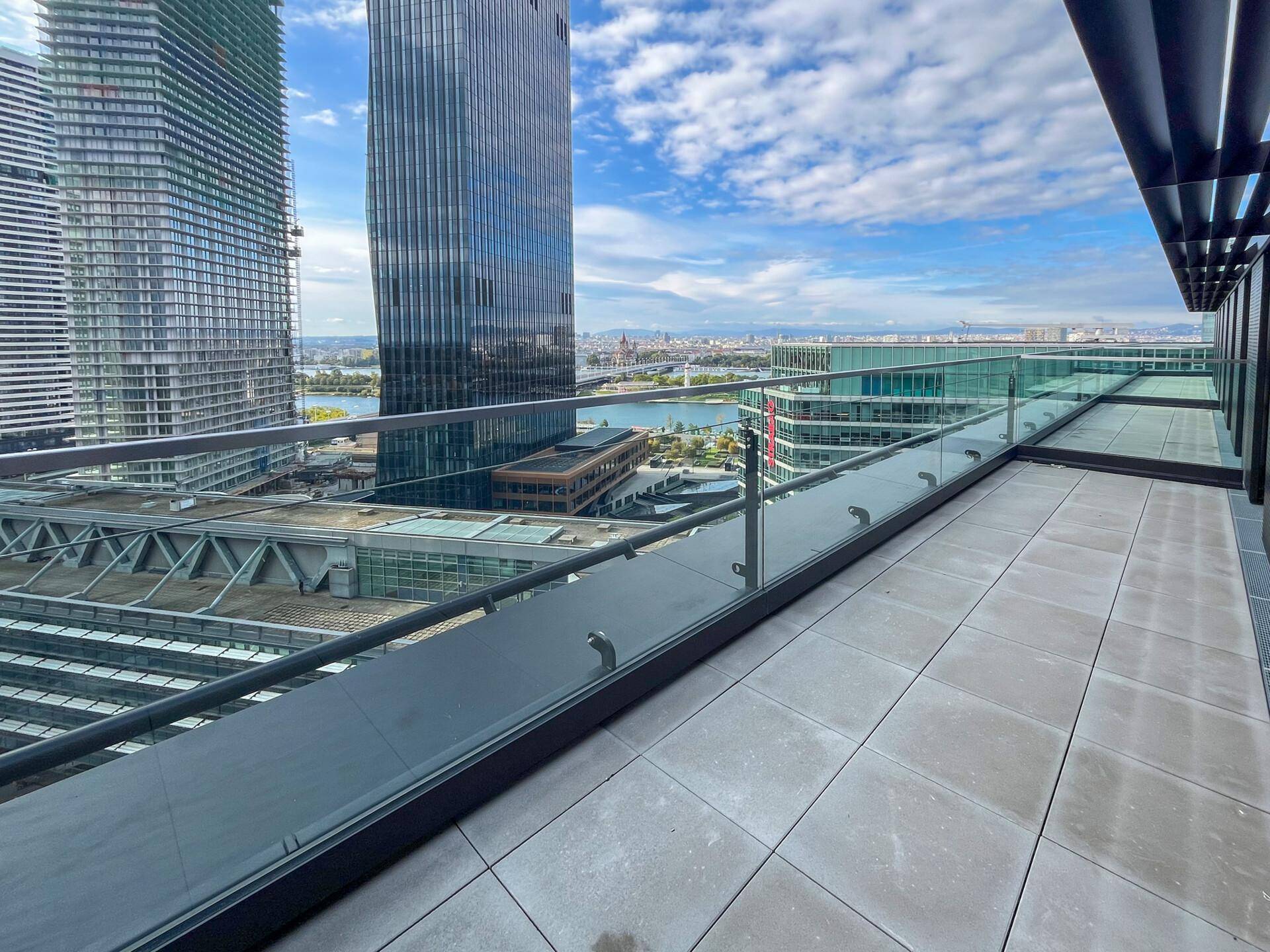 Geräumige Terrasse mit Fliesenboden und Glasgeländer, bietet einen weiten Blick auf die Stadt und das Wasser.