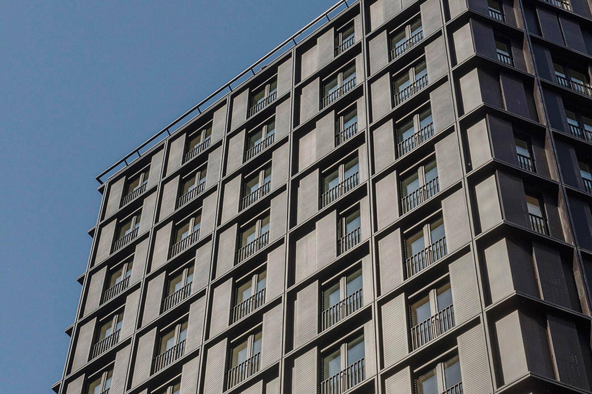 Fassadendetail eines modernen Hochhauses mit vielen Fenstern unter blauem Himmel.