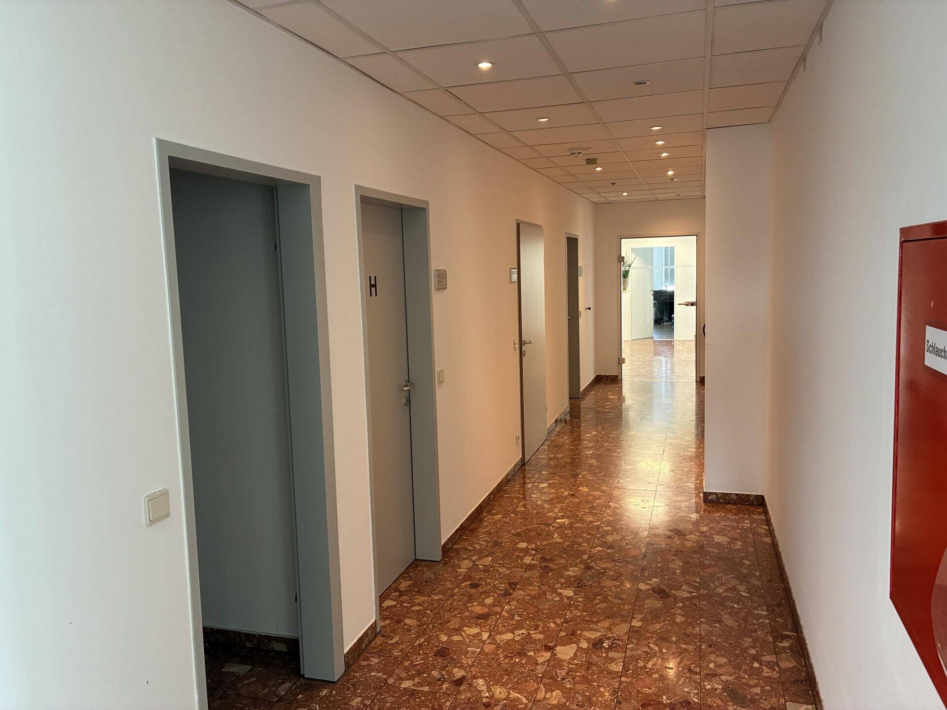 Langer Flur mit mehreren Türen, Terrazzo-Bodenfliesen und eingelassener Deckenbeleuchtung.