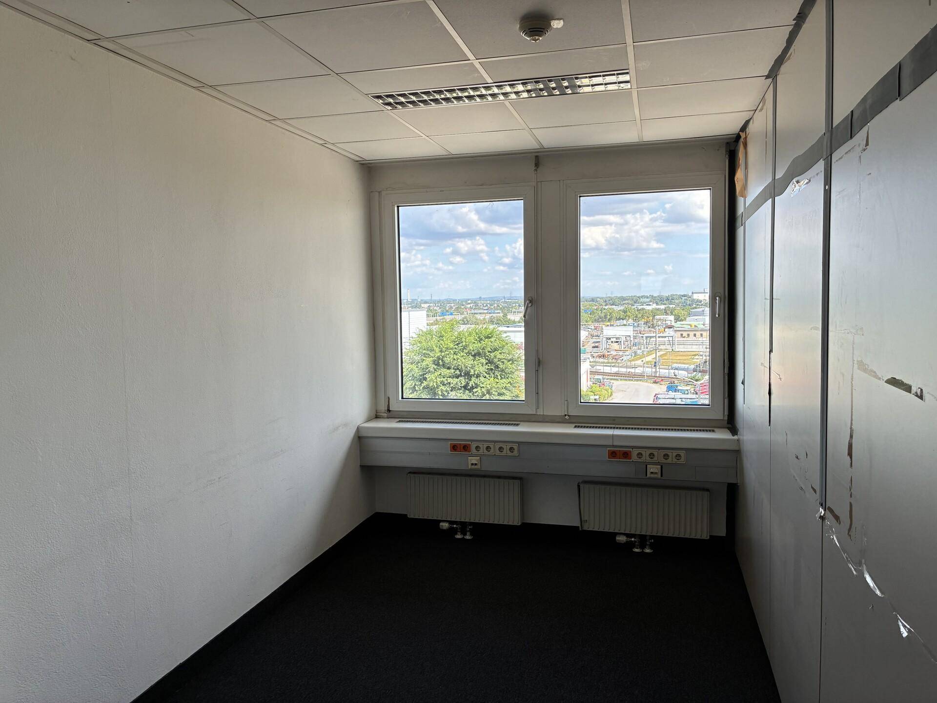Kleineres, leeres Büro mit zwei Fenstern, Teppichboden und modularen Wänden, bietet Ausblick.