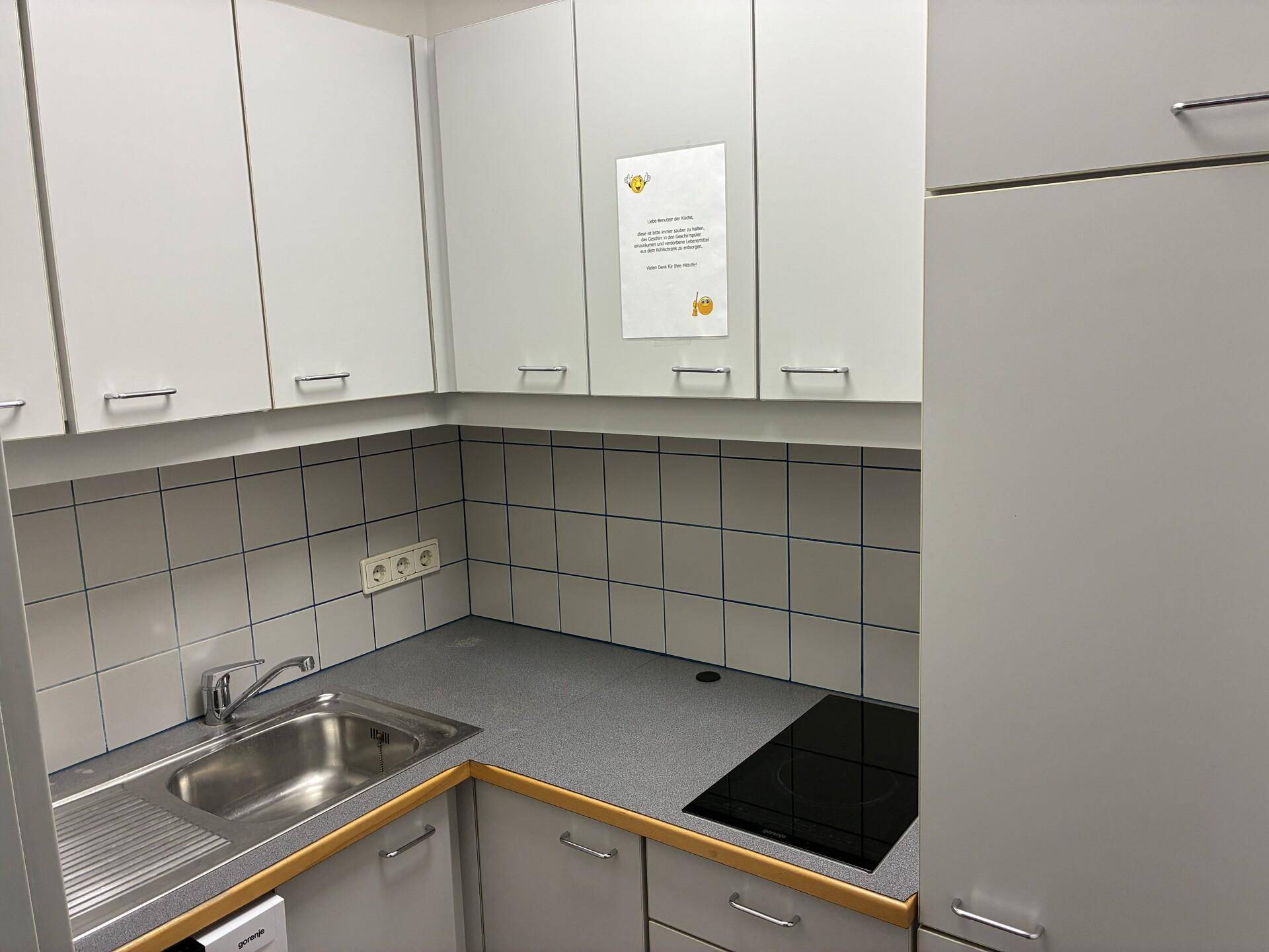 Kleine Küchenzeile mit weißen Schränken, Spüle, Induktionskochfeld und gefliestem Spritzschutz.