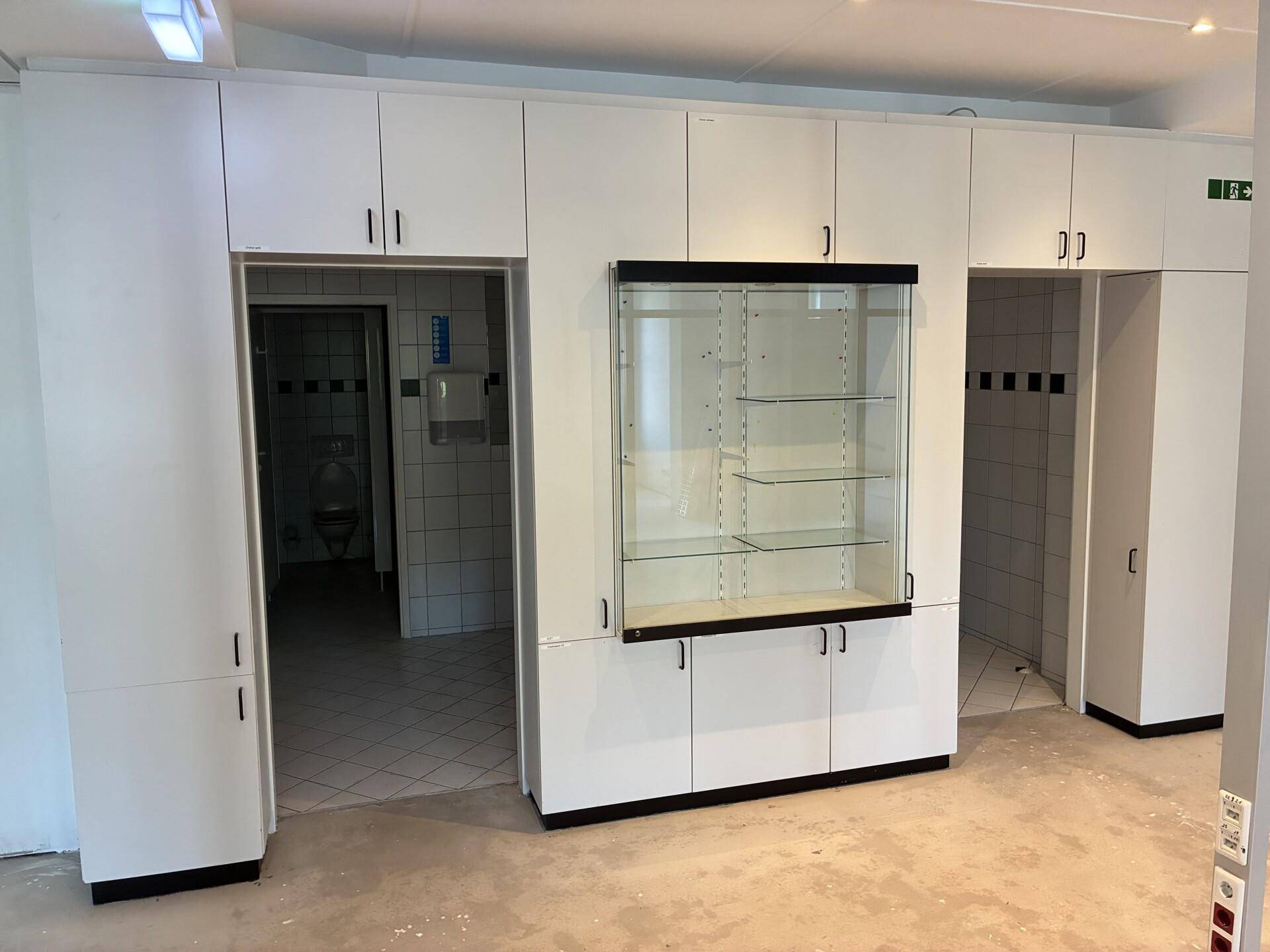 Flur mit weißen Einbauschränken, integrierter Vitrine und Zugang zu zwei Toilettenräumen.