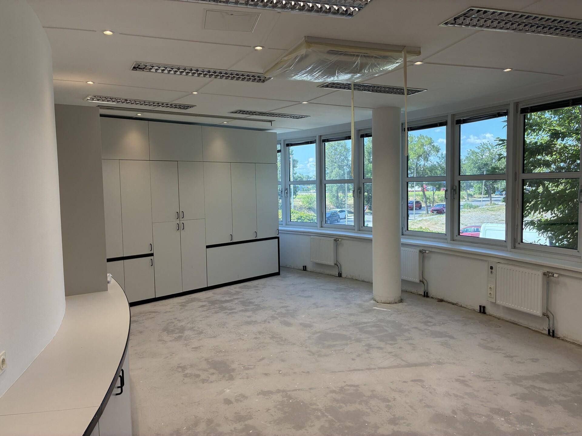 Helles Büro mit großen Fenstern, Einbauschränken und einem Betonboden, ideal für Arbeitsbereiche.