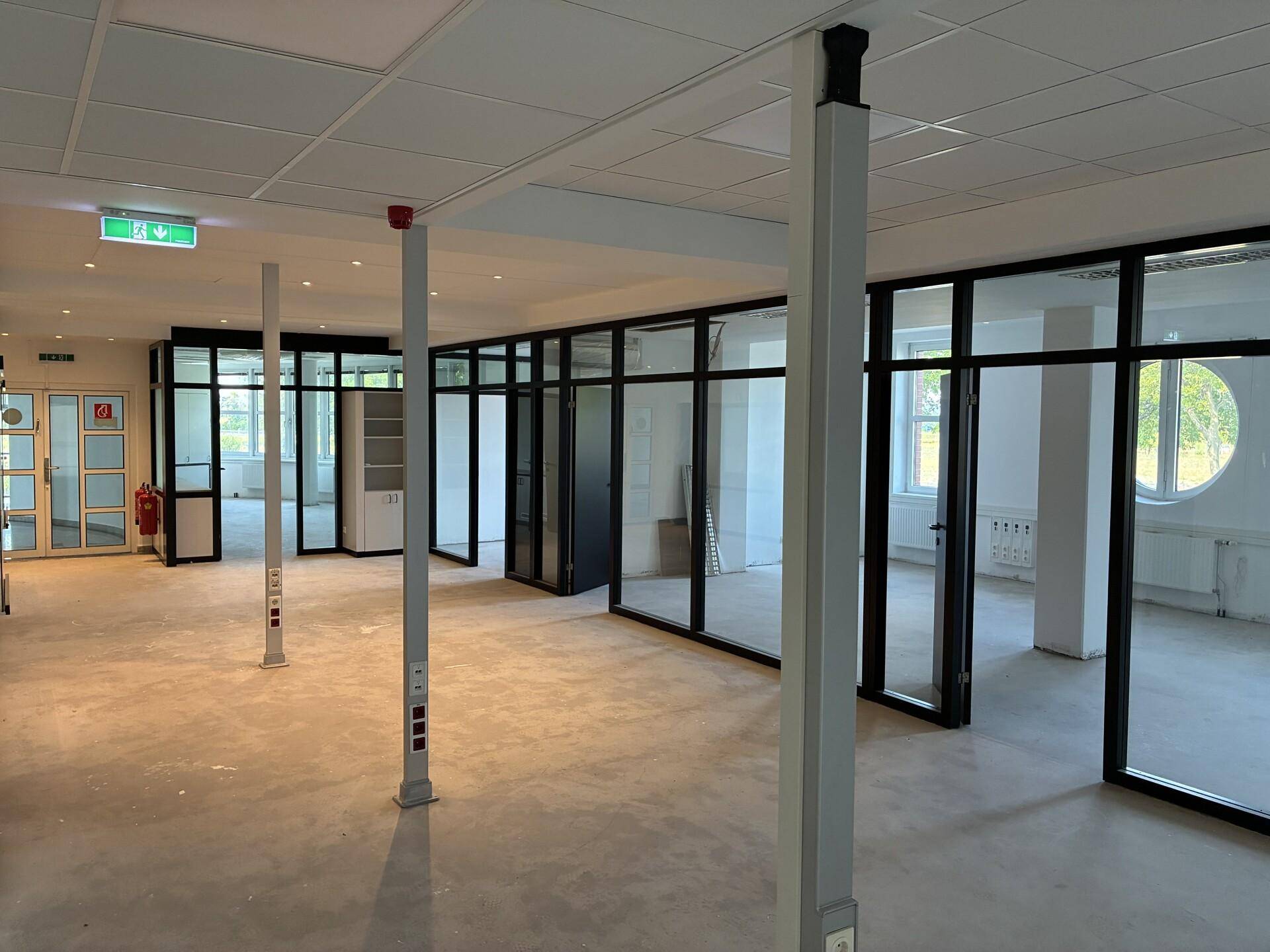 Großes Büro mit Glaswänden, Säulen und einem Betonboden, ideal für eine moderne Arbeitsumgebung.