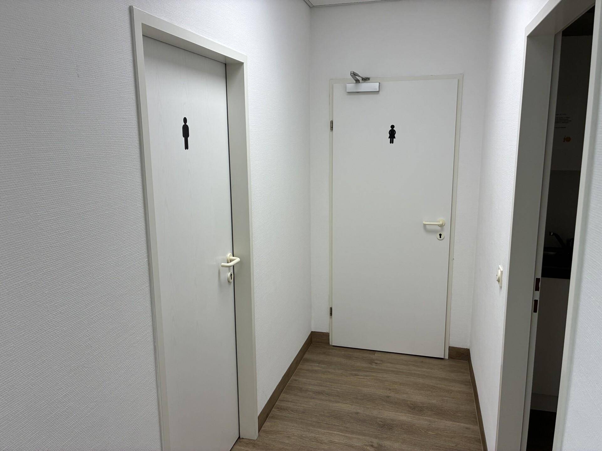 Flur mit zwei weißen Türen, die zu den getrennten Toiletten für Damen und Herren führen.