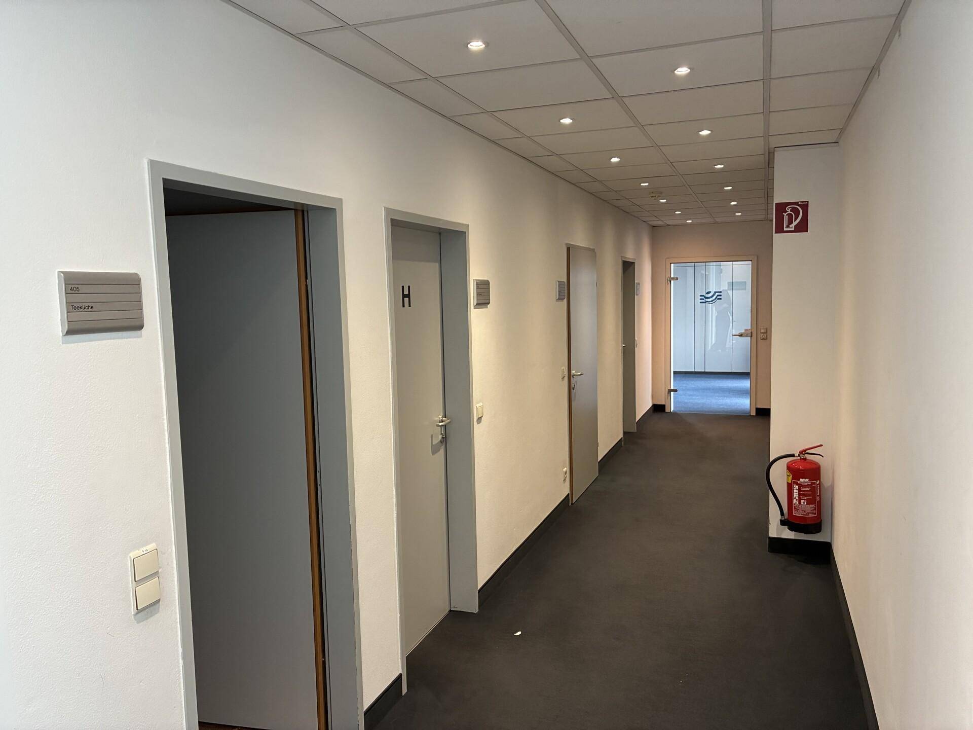 Langer, heller Flur mit mehreren Türen, Einbaustrahlern und einem Feuerlöscher an der Wand.