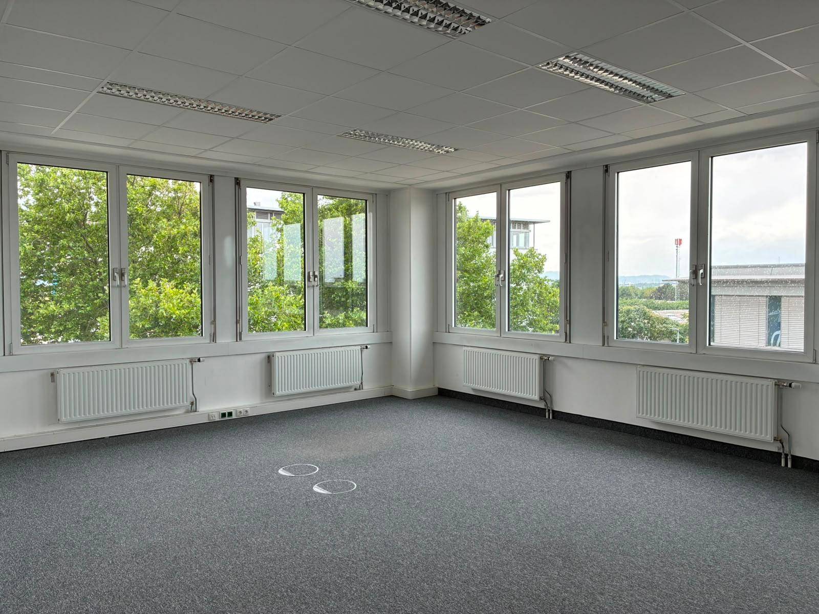 Geräumiges, leeres Büro mit vielen Fenstern, die viel Tageslicht hereinlassen und einen Ausblick bieten.