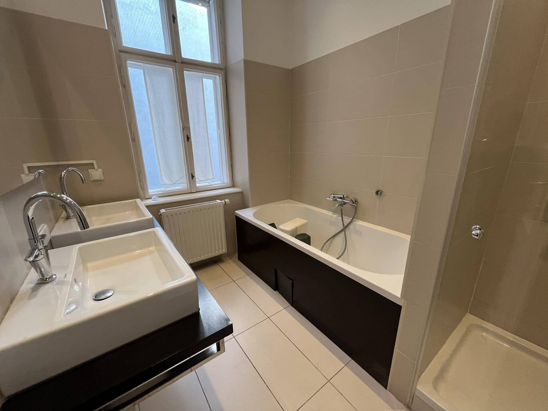 Modernes Badezimmer mit Doppelwaschbecken, Badewanne und separater Dusche, hell gefliest.
