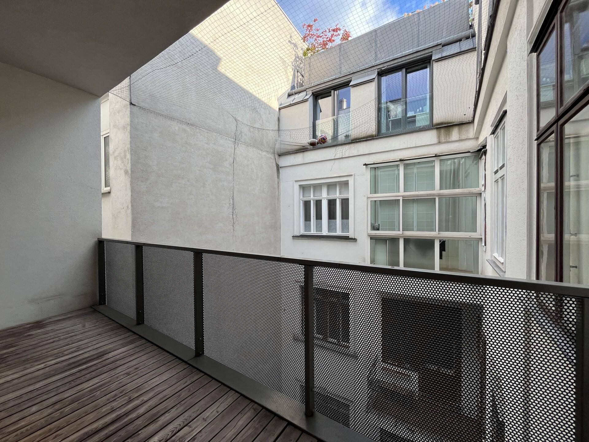 Balkon mit Holzboden und Blick auf den Innenhof, umgeben von Gebäuden.