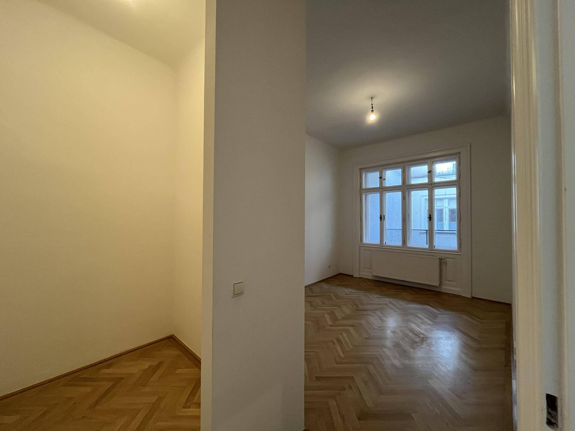 Innenraum mit Fischgrätparkett und Blick in ein weiteres helles Zimmer.