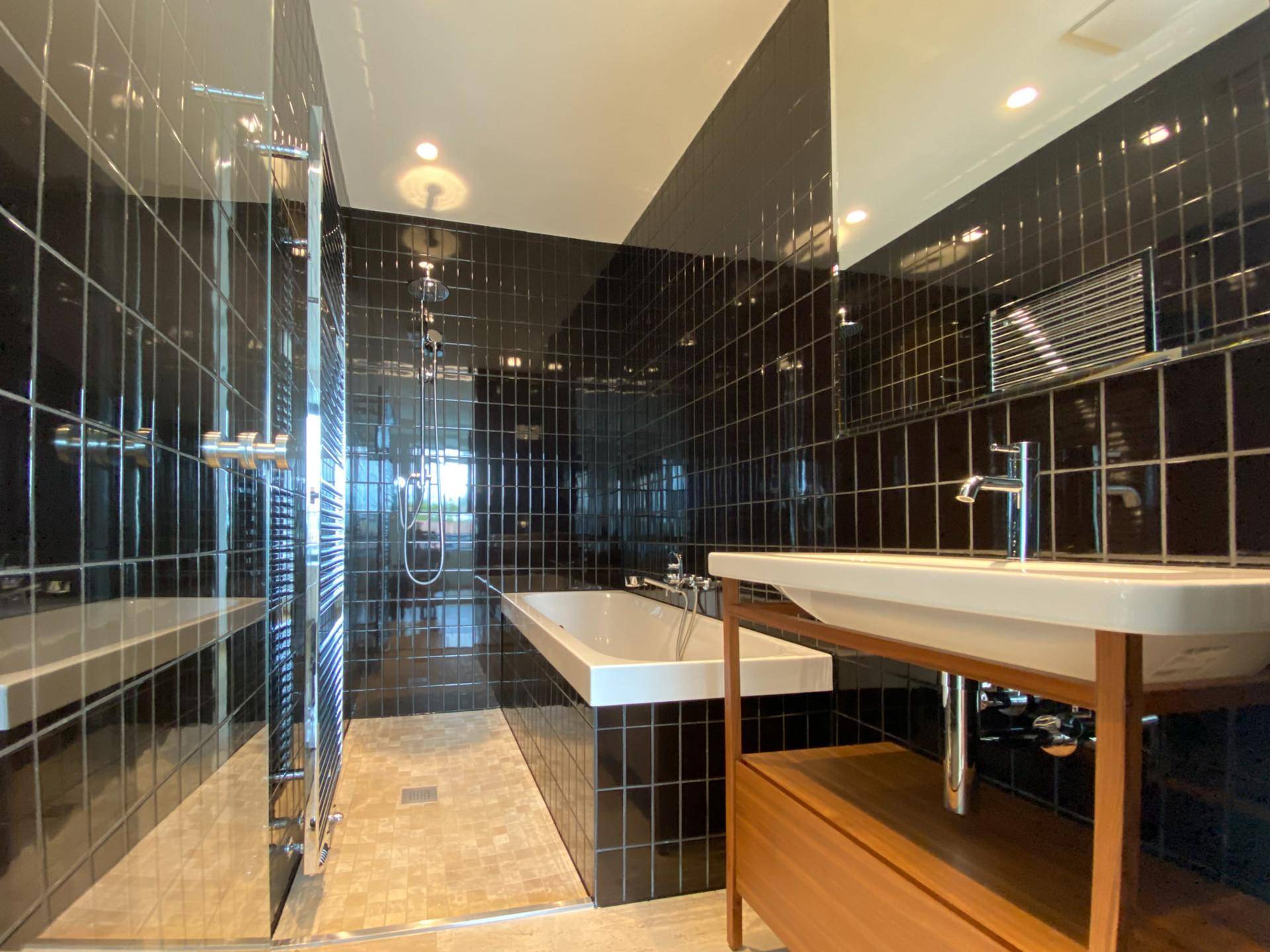 Modernes Badezimmer mit schwarzen Fliesen, Badewanne und begehbarer Dusche.
