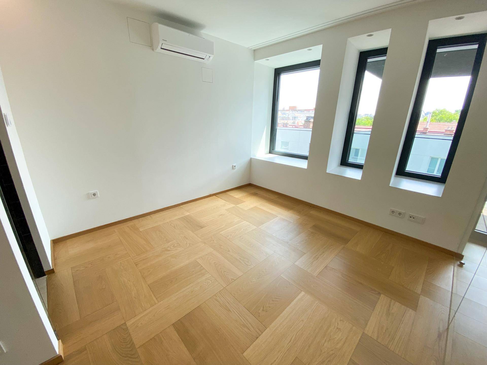 Helles Schlafzimmer mit Fischgrätparkett, Klimaanlage und mehreren Fenstern für viel Tageslicht.