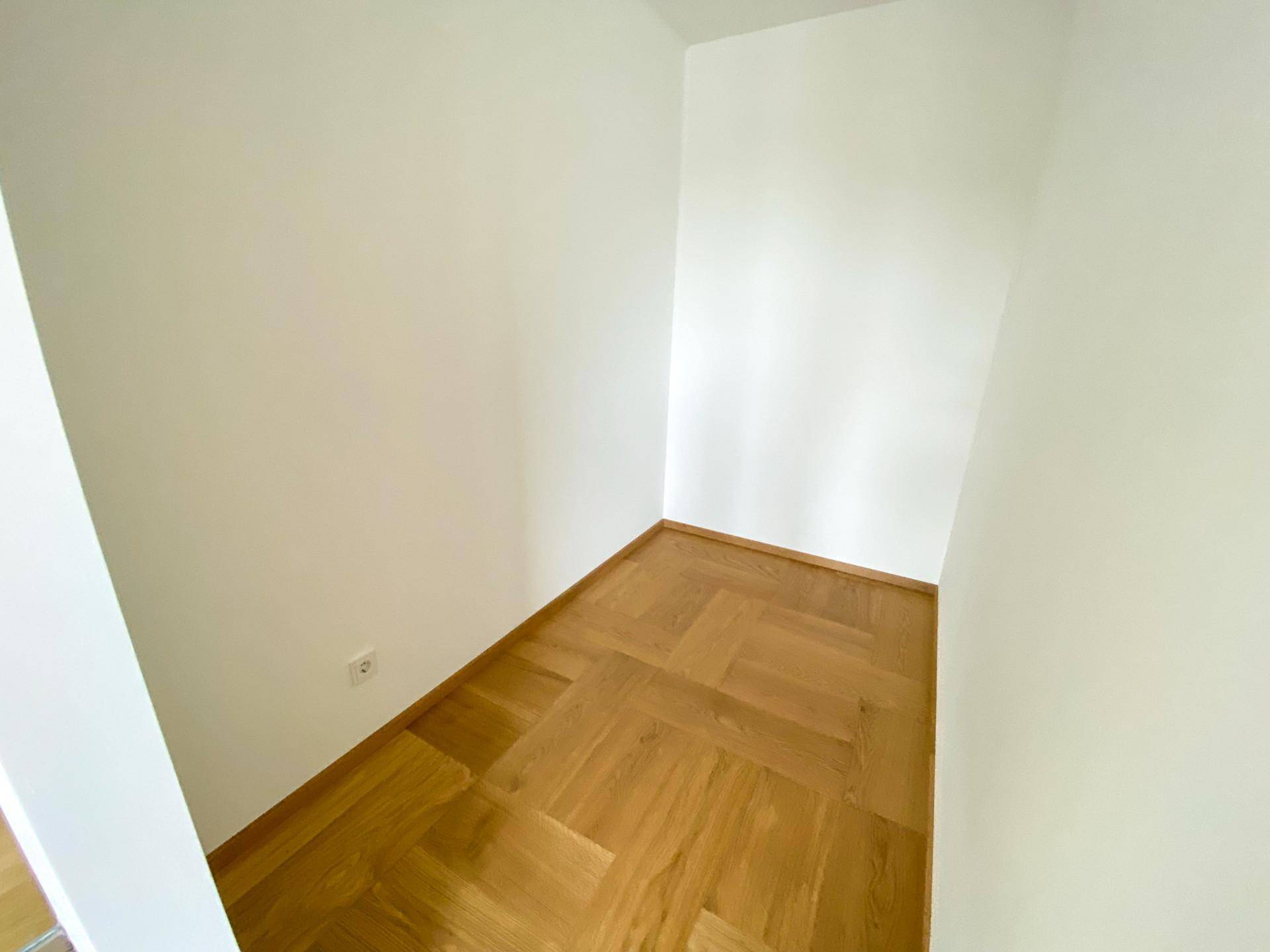 Kleiner, heller Raum mit Fischgrätparkett und weißen Wänden, ideal als Abstellraum.