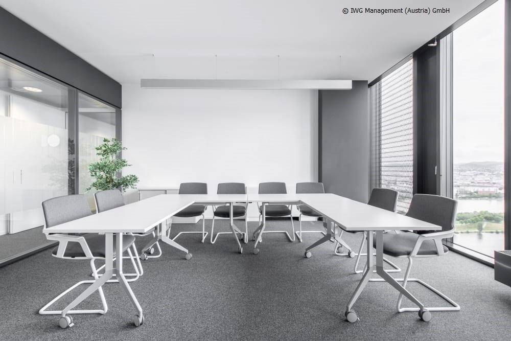 Heller Konferenzraum mit U-förmigem Tisch und ergonomischen Stühlen, bietet Blick auf die Stadt.