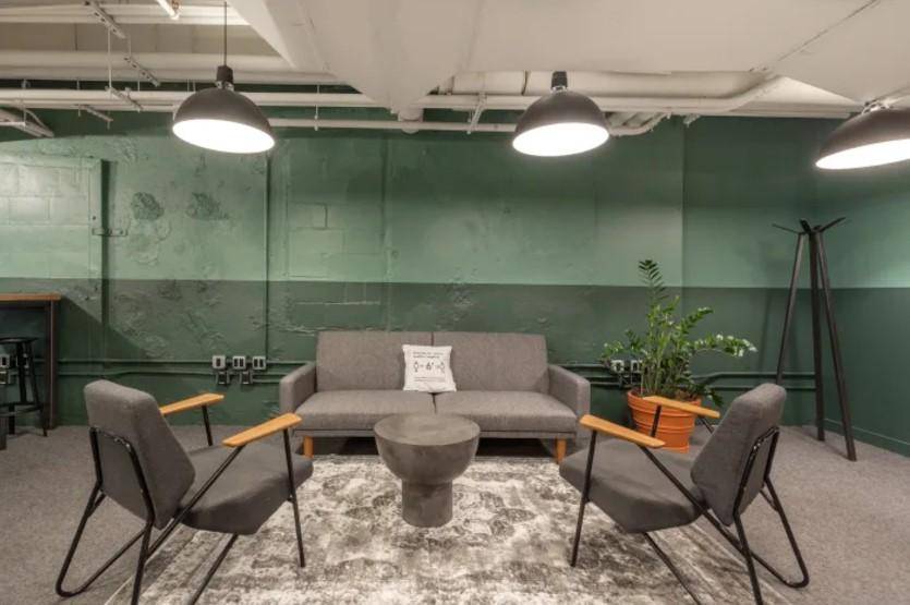 Gemütlicher Loungebereich mit grauen Sofas, Teppich und zweifarbigen grünen Wänden im Industriestil.