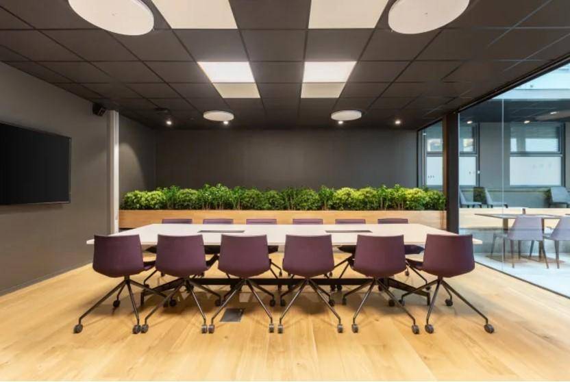 Eleganter Konferenzraum mit Holzboden, langer Tafel und einer grünen Pflanzenwand als Akzent.