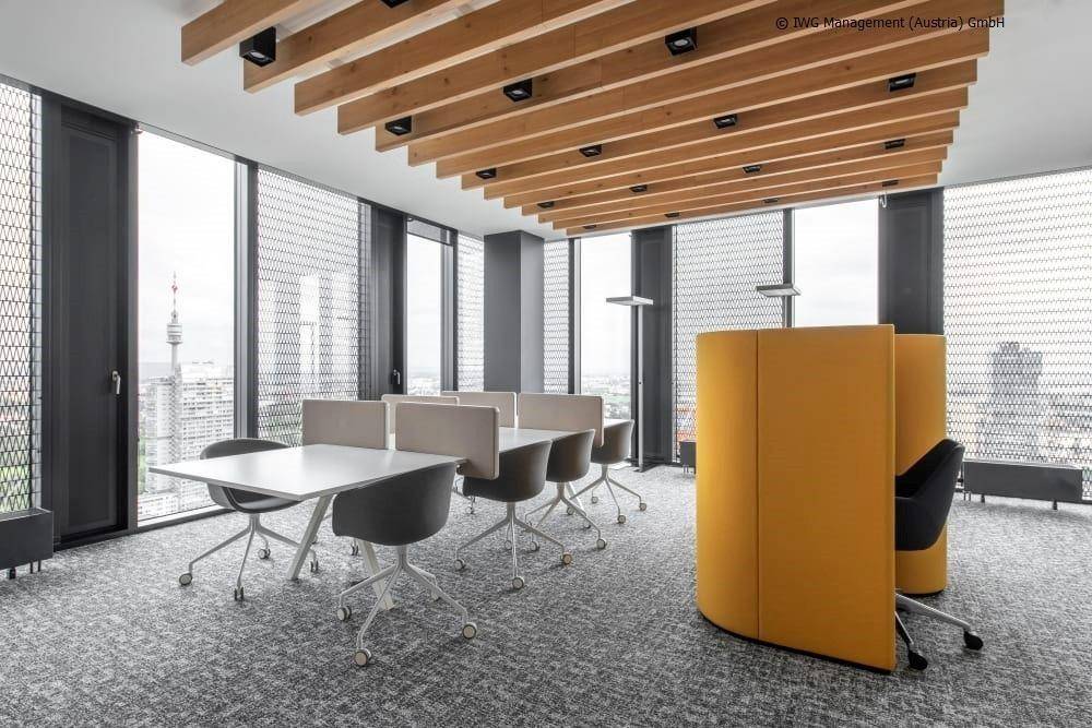 Modernes Großraumbüro mit Holzbalkendecke, ergonomischen Arbeitsplätzen und Stadtblick.