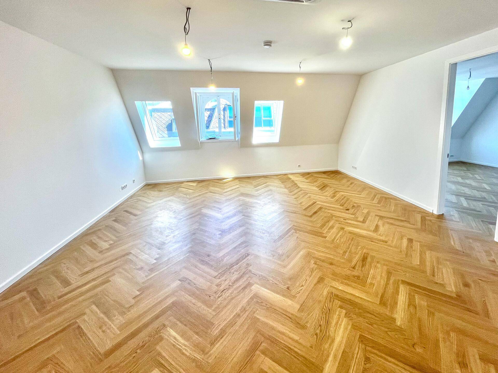 Geräumiges Zimmer mit elegantem Fischgrätparkett, Dachschrägen und viel Tageslicht durch die Dachfenster.